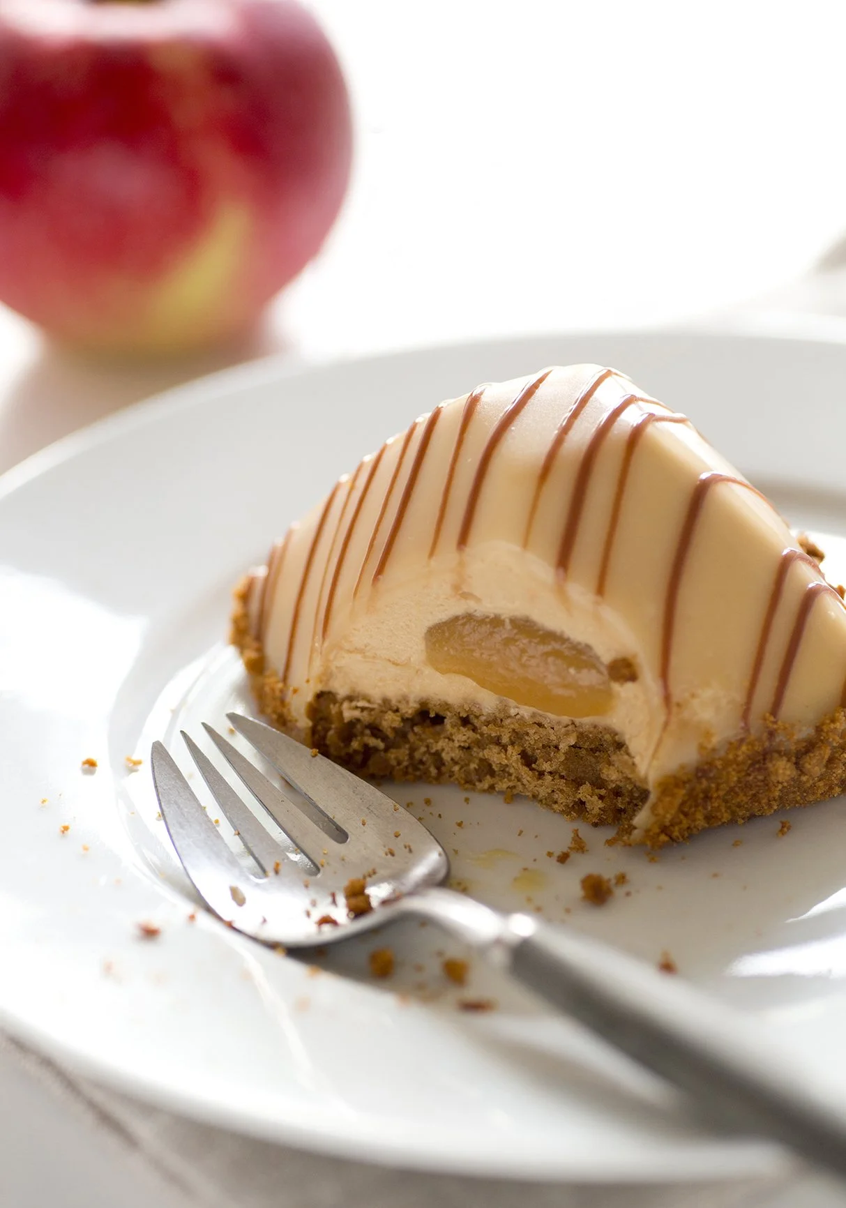 Apple french pastry with apple compote heart and caramel mousse, on white plate with fork and out of focus apple in the background