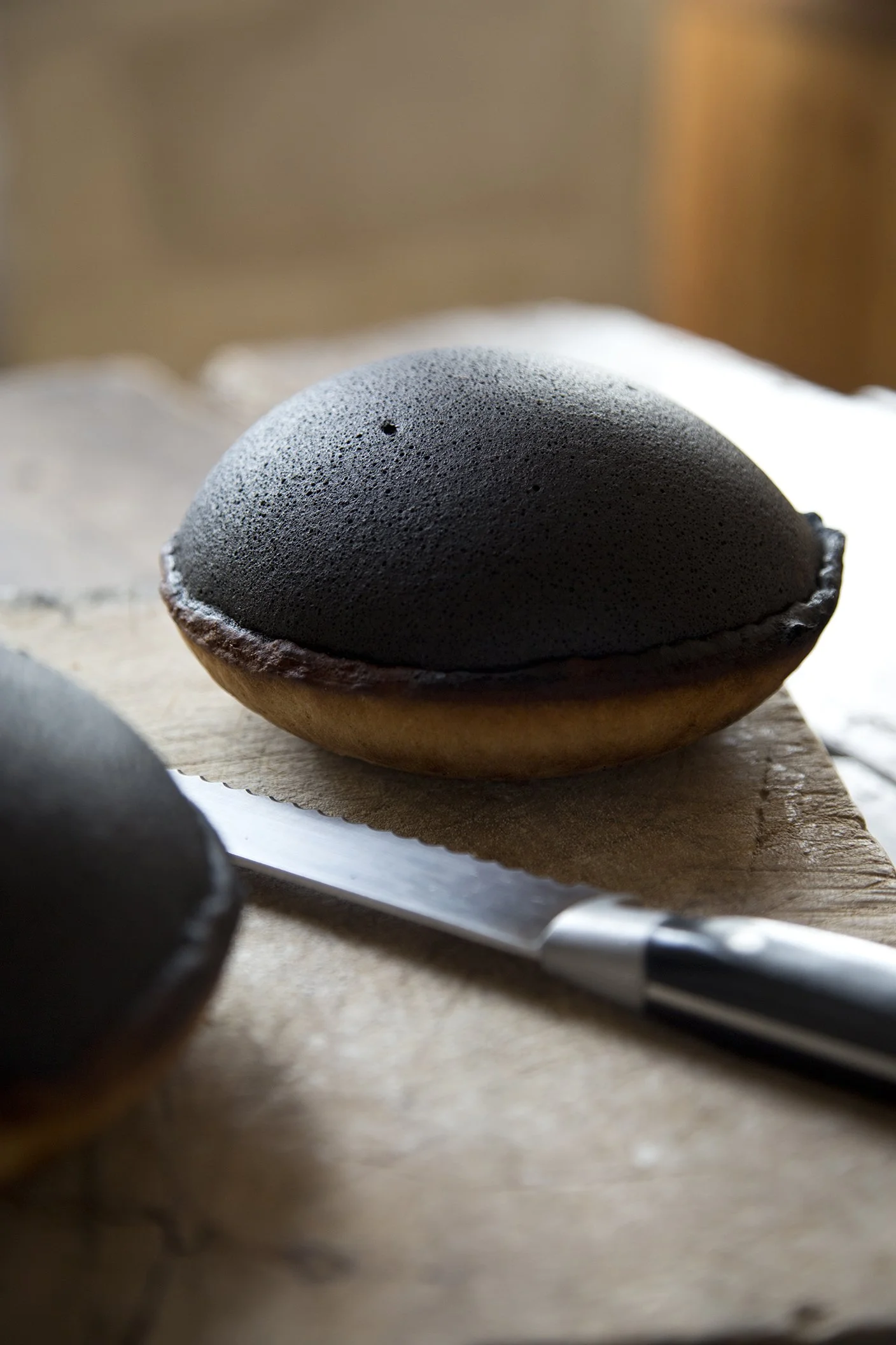 Close-up of a domed, deeply caramelized tourteau fromager next to a serrated knife, a French goat cheese cake specialty.