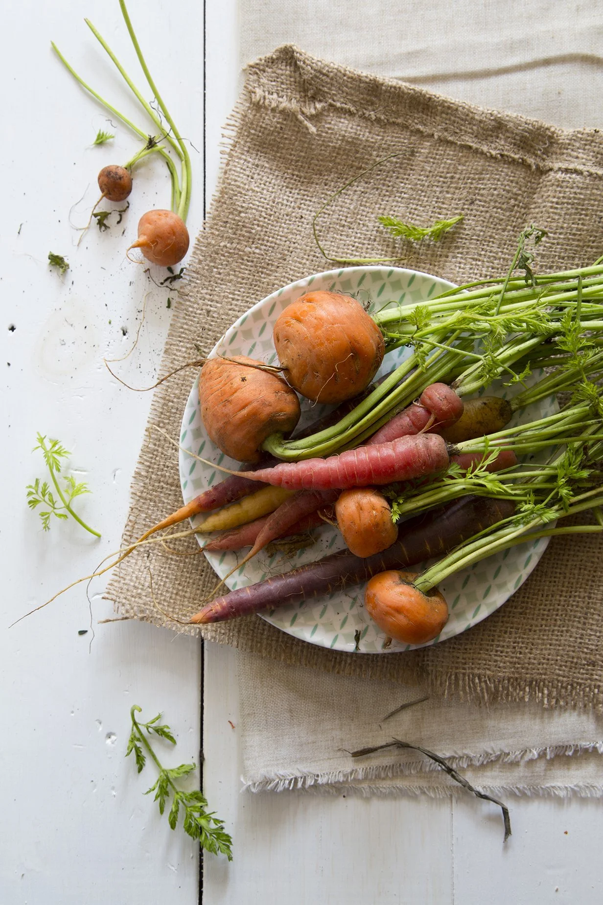 Heirloom carrots and round baby beets with their greens still attached, arranged on a plate over burlap.

