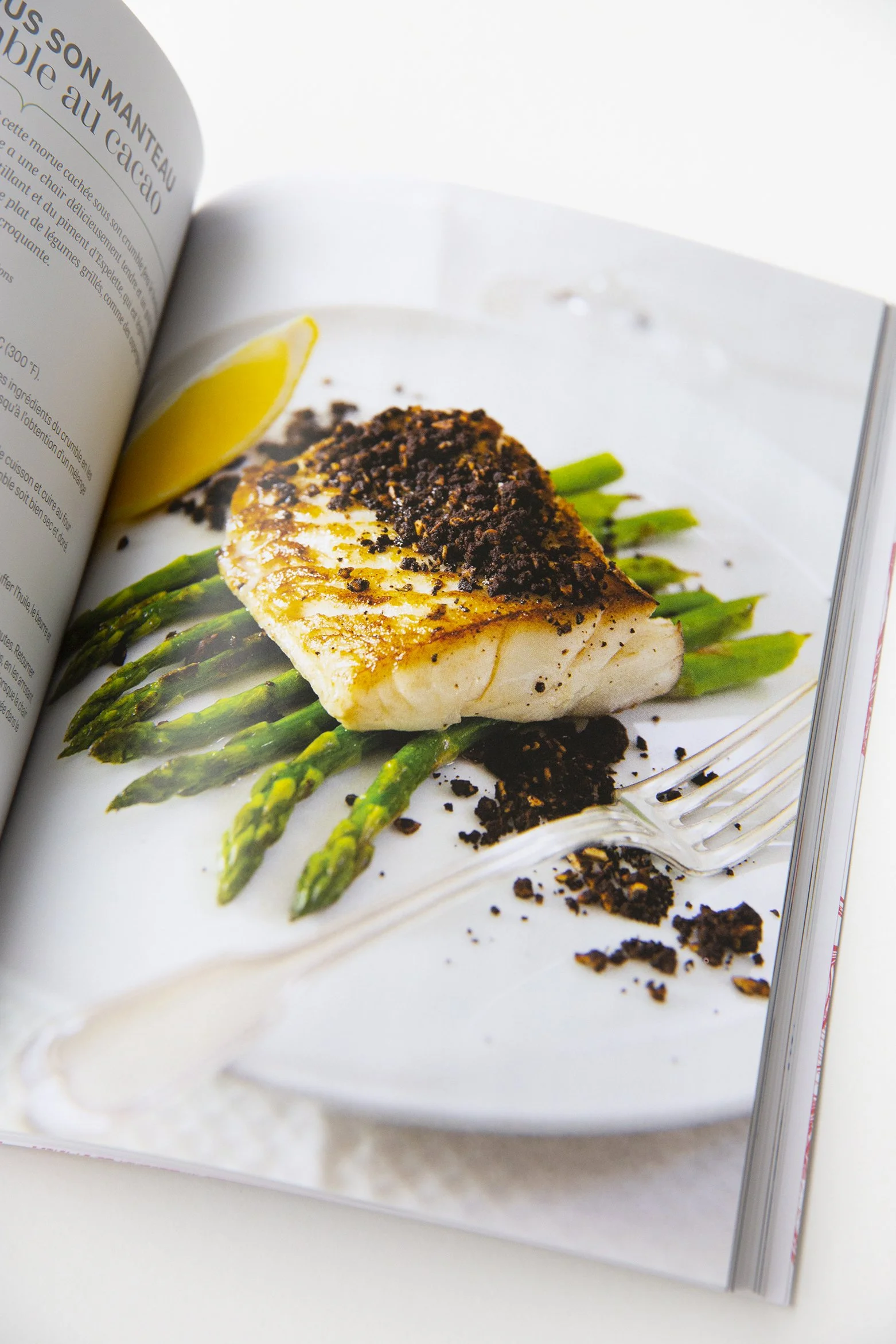 Cookbook opened on a page with a recipe of a cocoa crusted salmon on asparagus