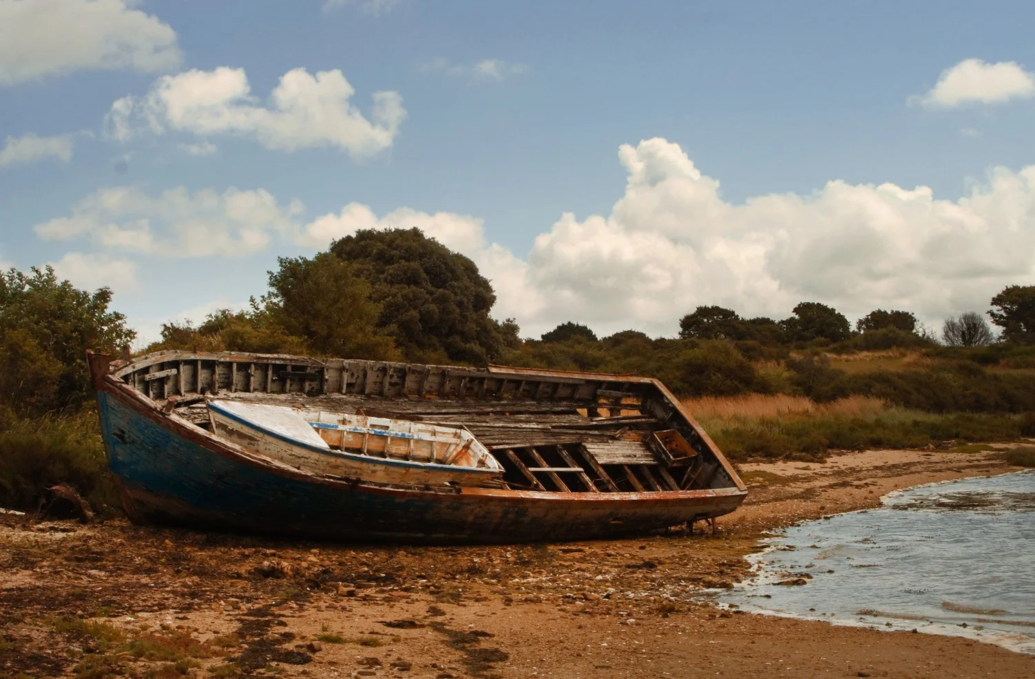 Abandoned boat on French beach, beautiful composition and saturated colors, sand, sea and sky. 