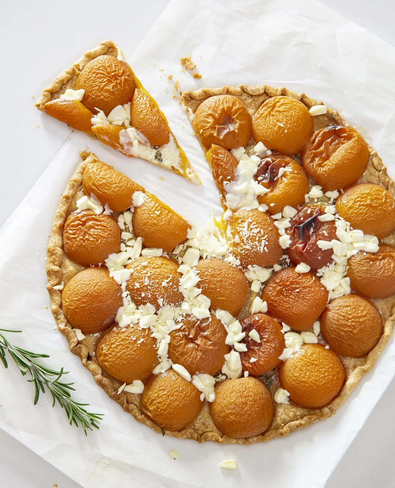Apricot and white chocolate tart, overhead shot, with sprig of rosemary on white background