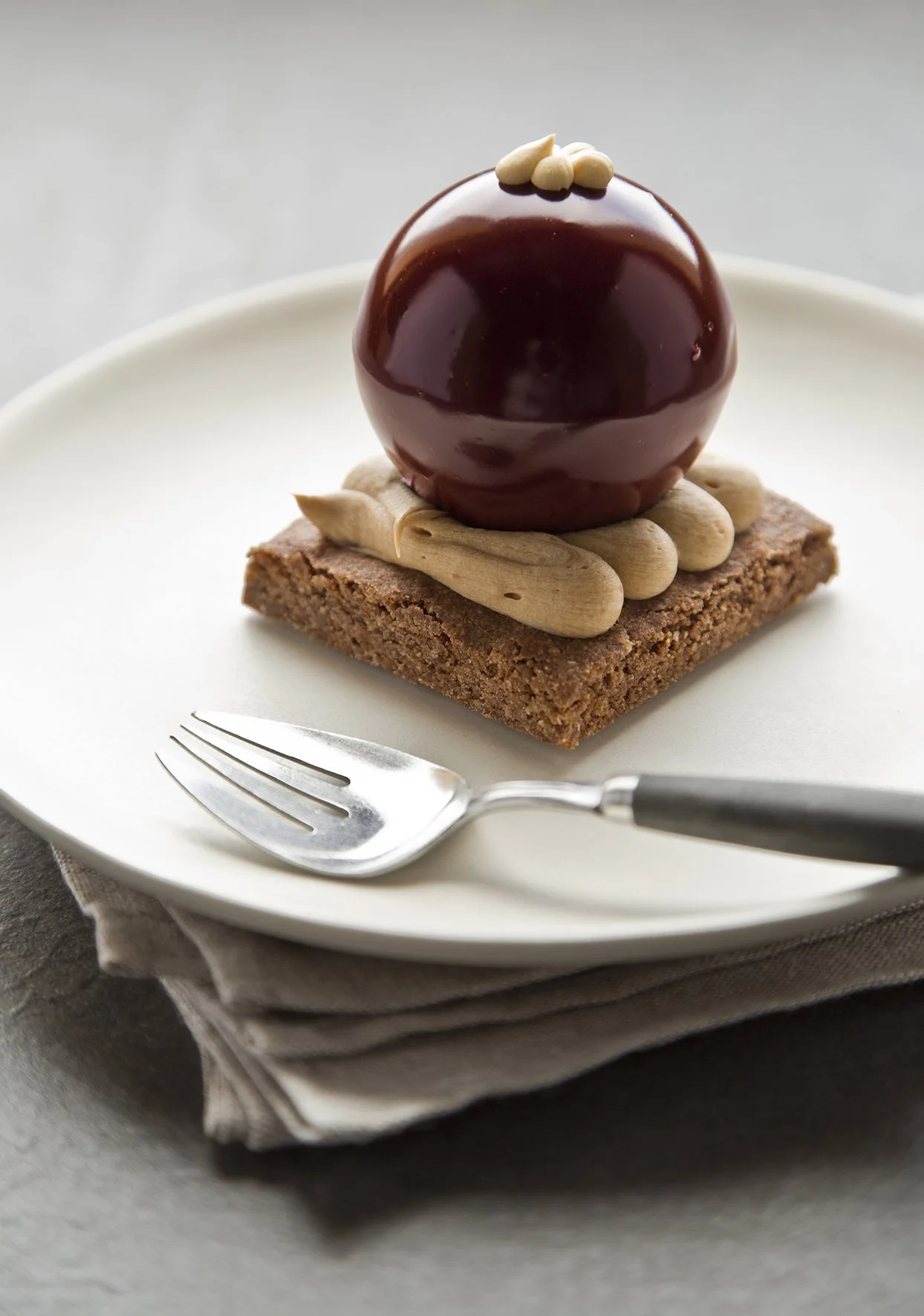 Shiny dark red chocolate pastry shaped like a Christmas ornament on crunchy cookie base and chocolate mousse