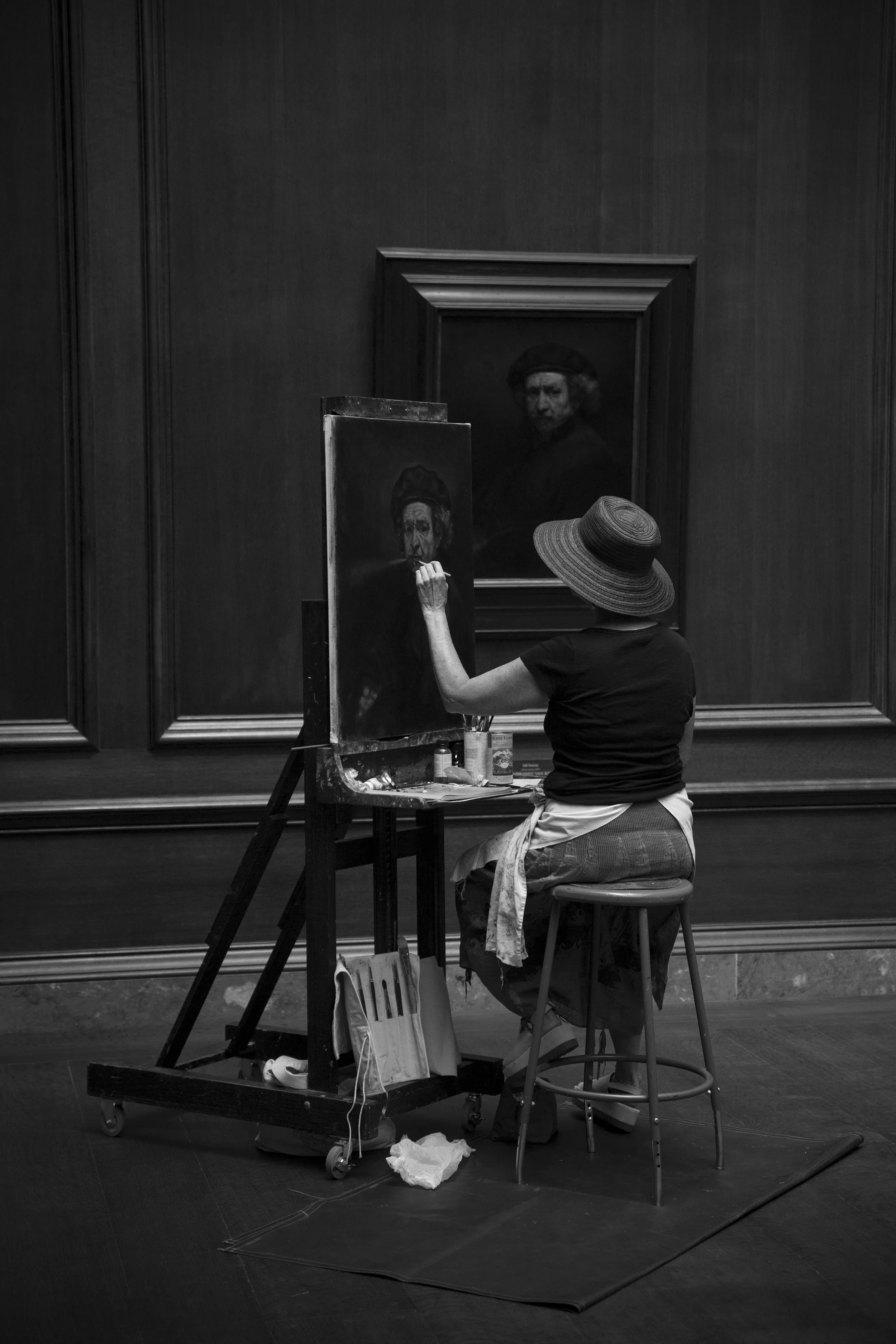 Fine art painter cipying a Rembrandt self portrait in an art museum, moody and solitary black and white photography. 