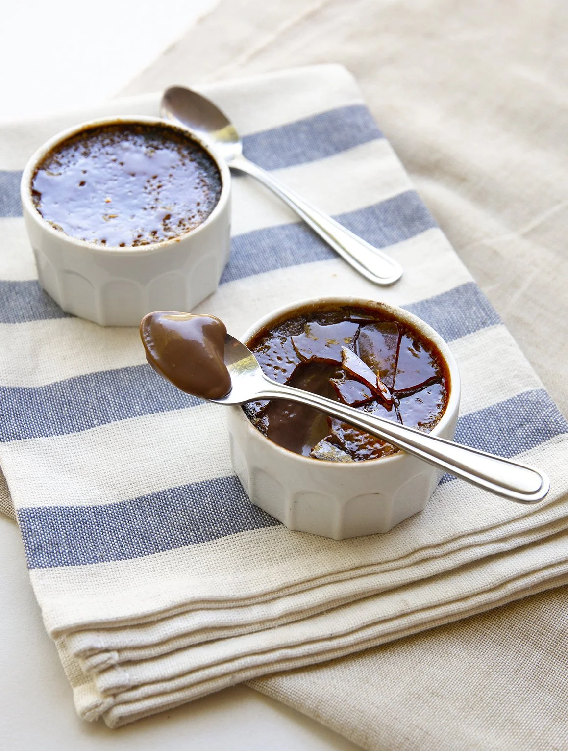 Chocolate creme brulee pots on striped white and blue cloth, with crunchy caramale and silver spoon