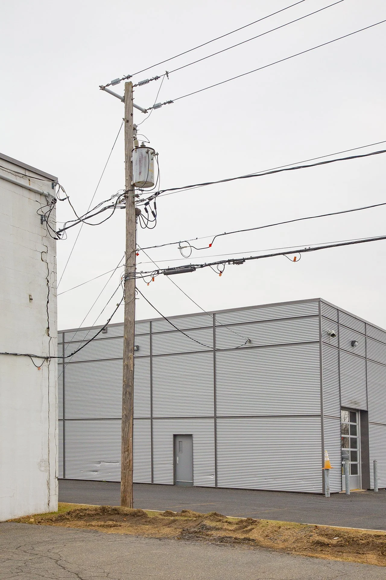 Art photo of everyday beauty. Wooden power pole with tangled wires against a corrugated metal warehouse under flat grey sky. 