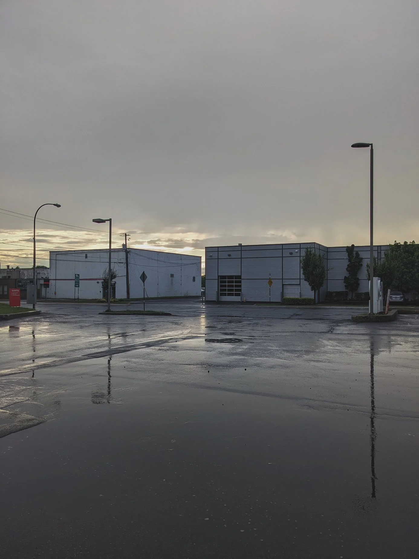 Rain-soaked industrial parking lot at dusk reflecting streetlights and a break of sky, Montreal. From a series on suburban moods and places. 