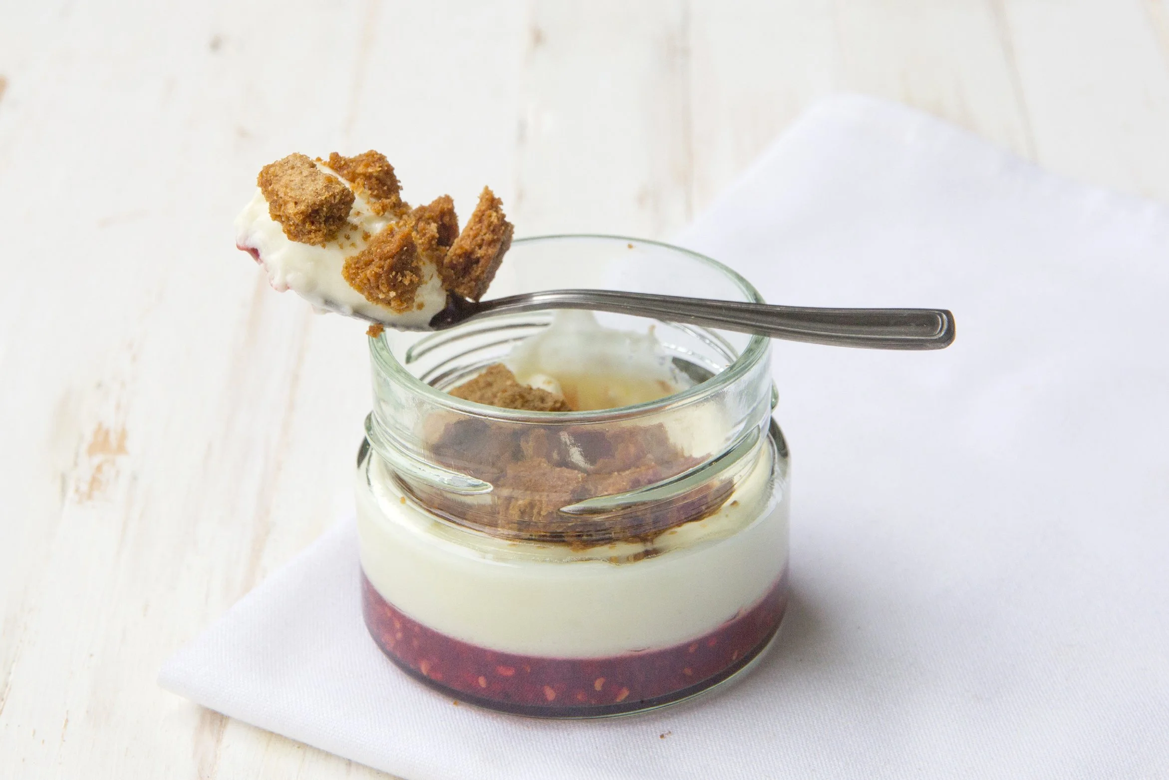 Raspberry cheesecake in a jar, with spoon and cookie crumble on top.