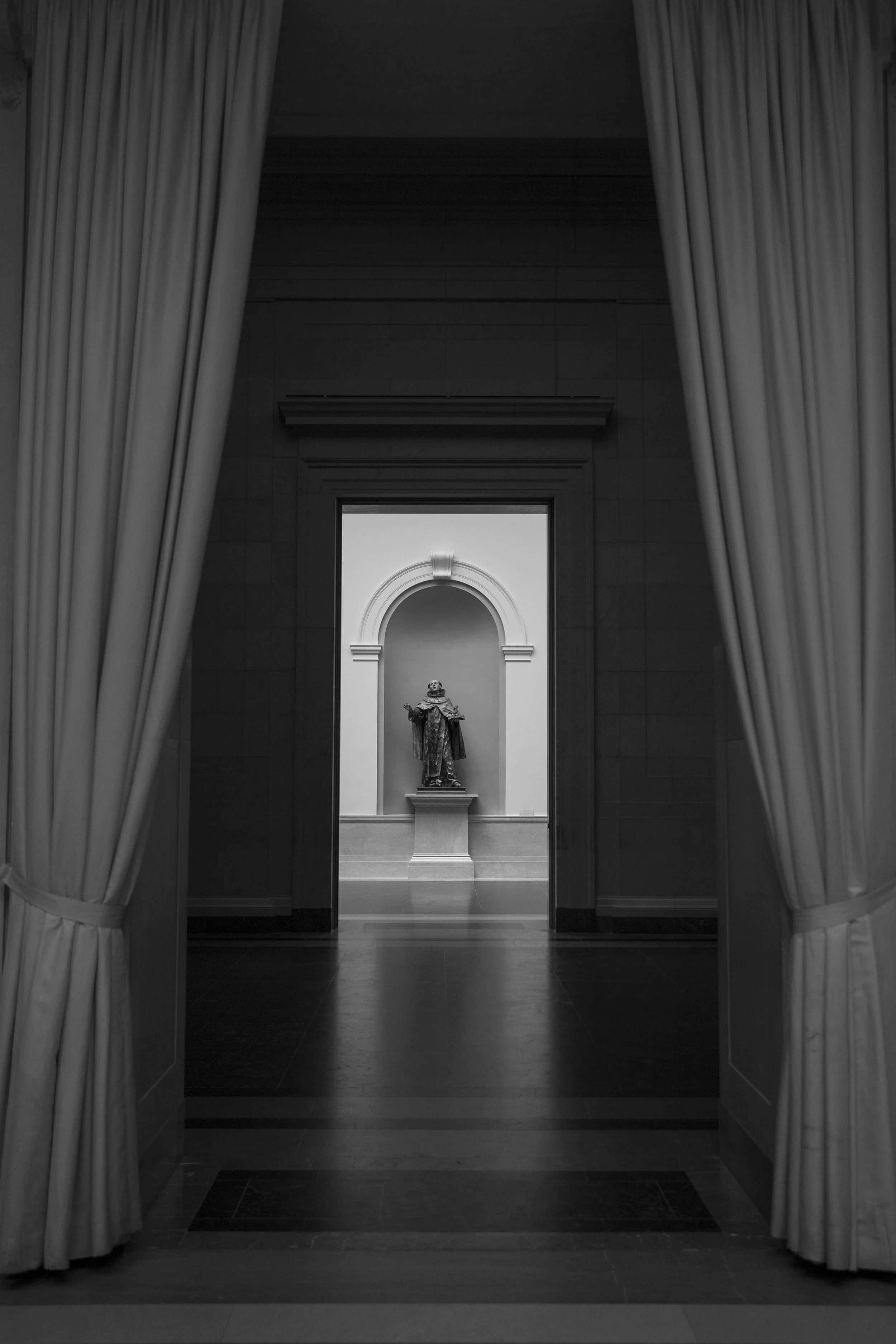 Vista inside an art museum, with series of rooms with contrasting lighting captured on black and white architectural phpto by Lionel May