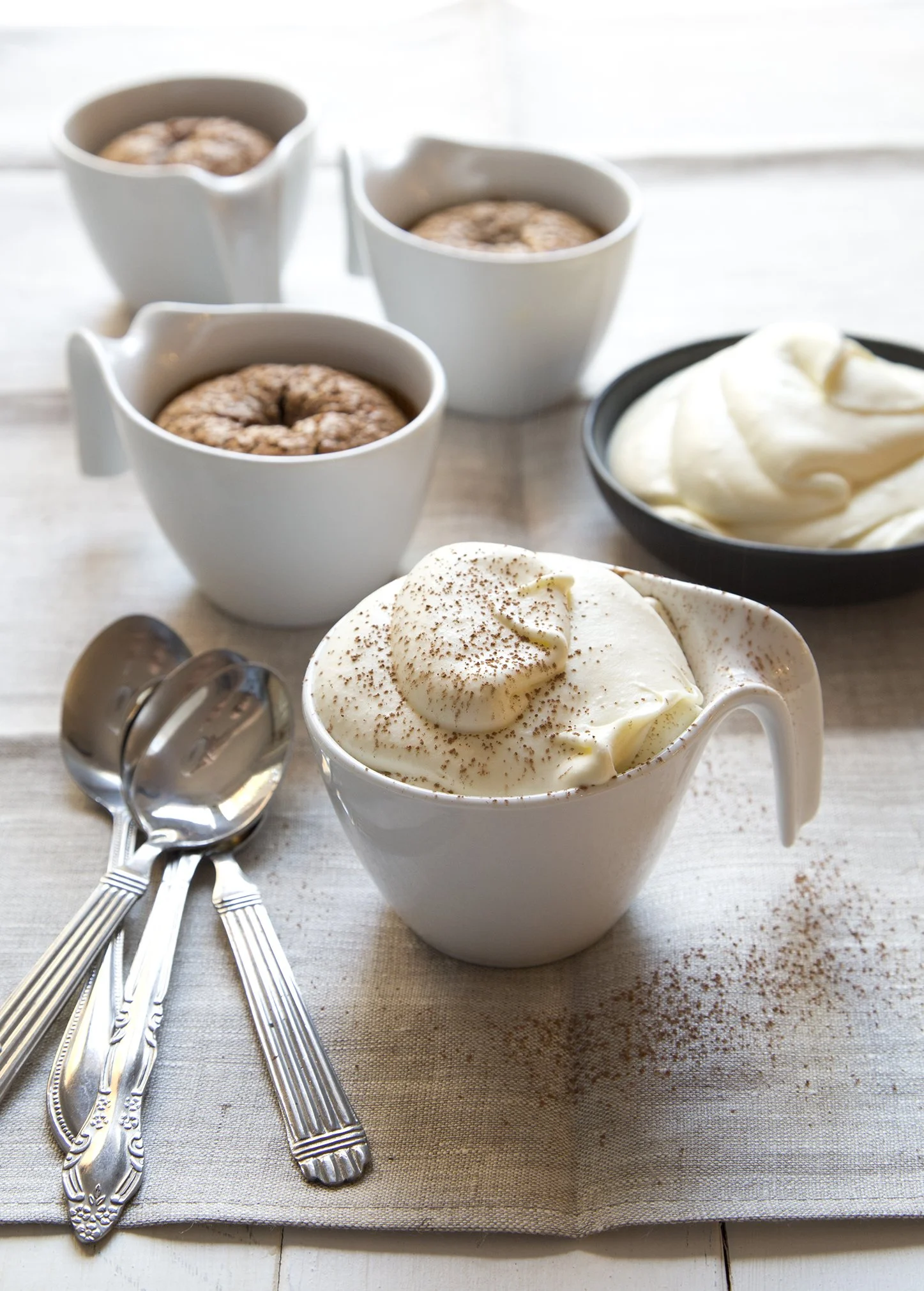 Tiramisu brownies baked in white porcelain cups and topped with whipped cream and dusted with cocoa. 