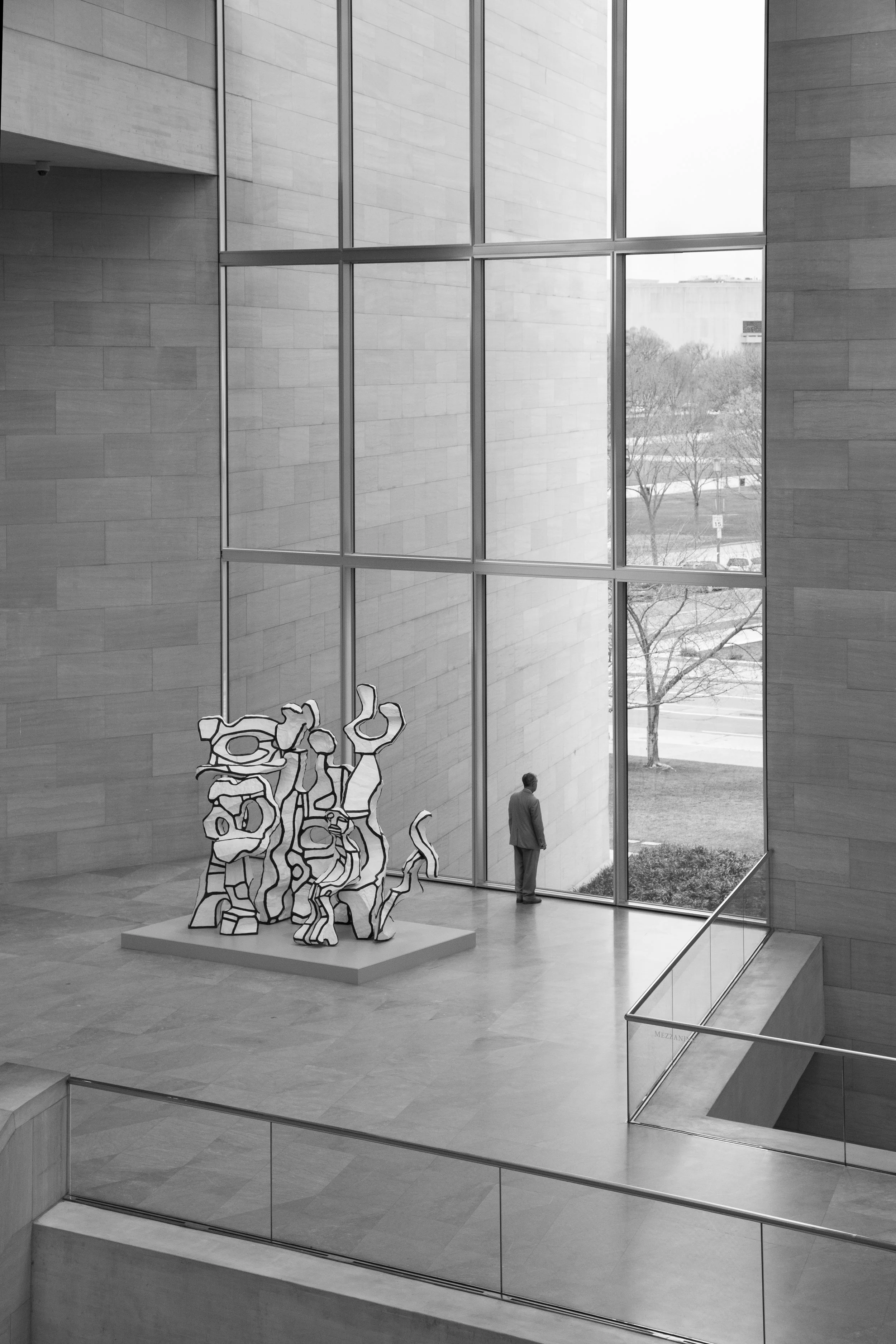 Beautifully composed black and white photo of the National Gallery Museum in Washington DC, with solitary man staring out a bay window