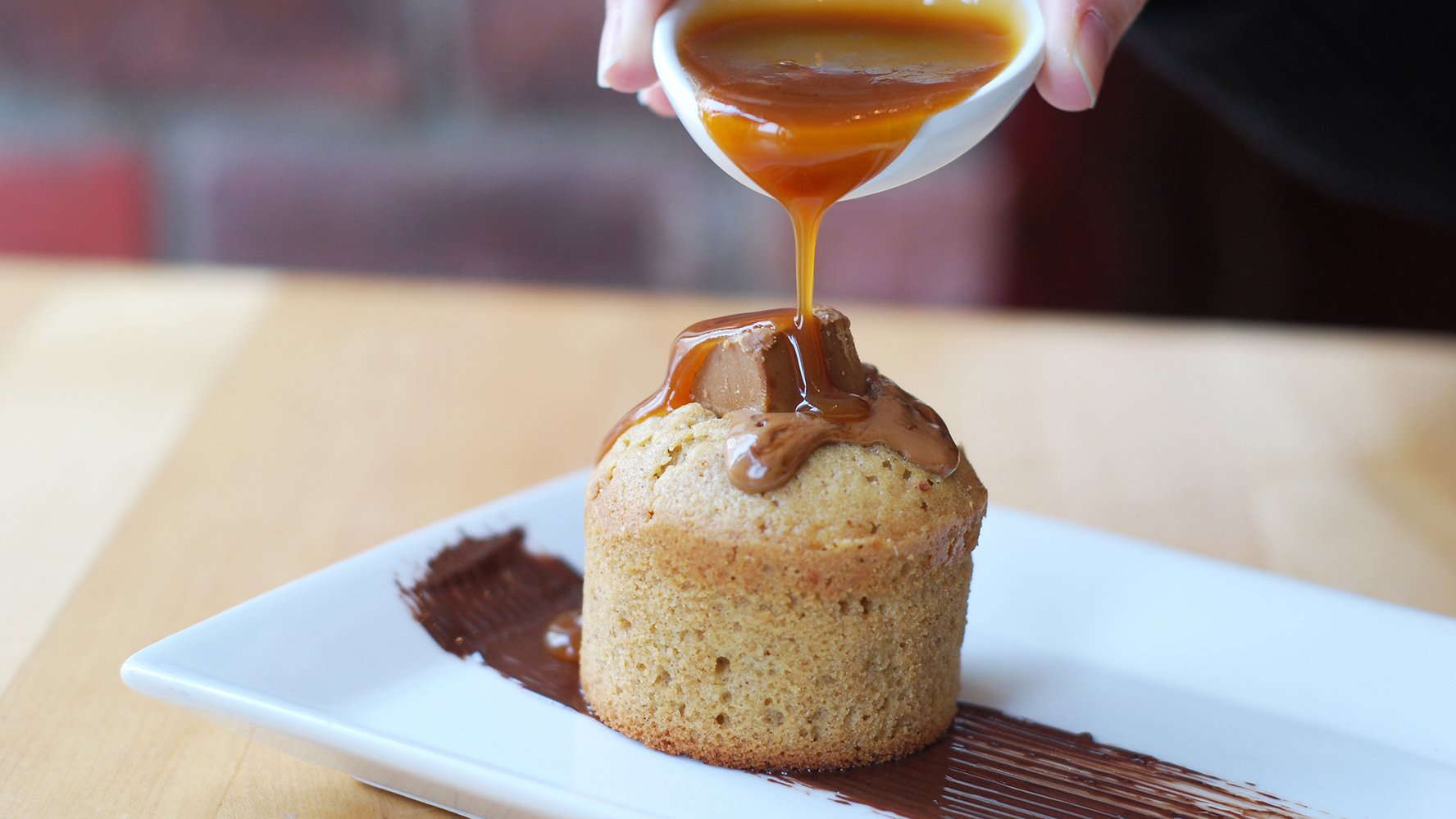 A white chocolate and caramel molten heart cake with a hand pouring slated caramel on top