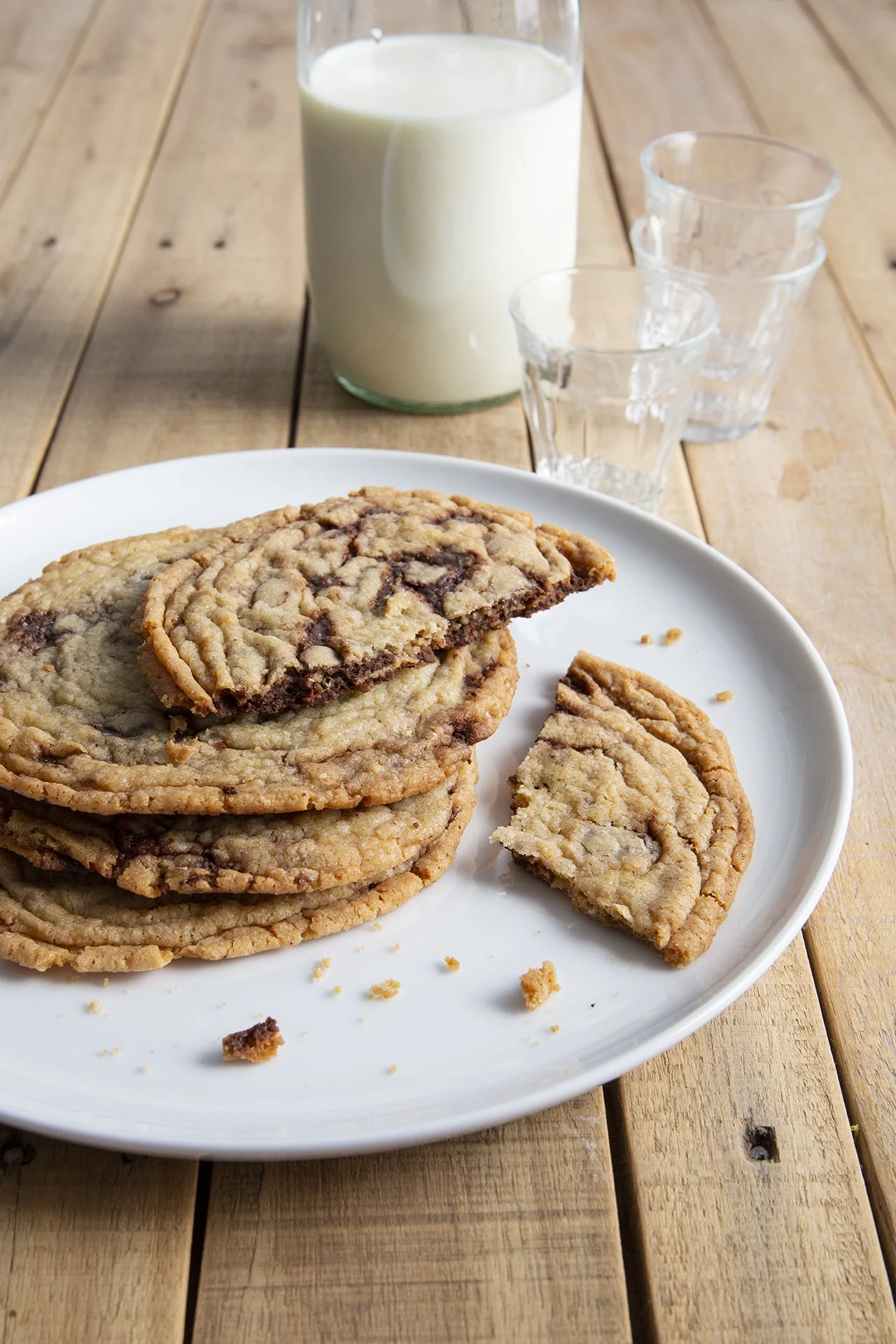 Thin crispy chocolate chip cookies on a serving plate with a glass of milk in the background