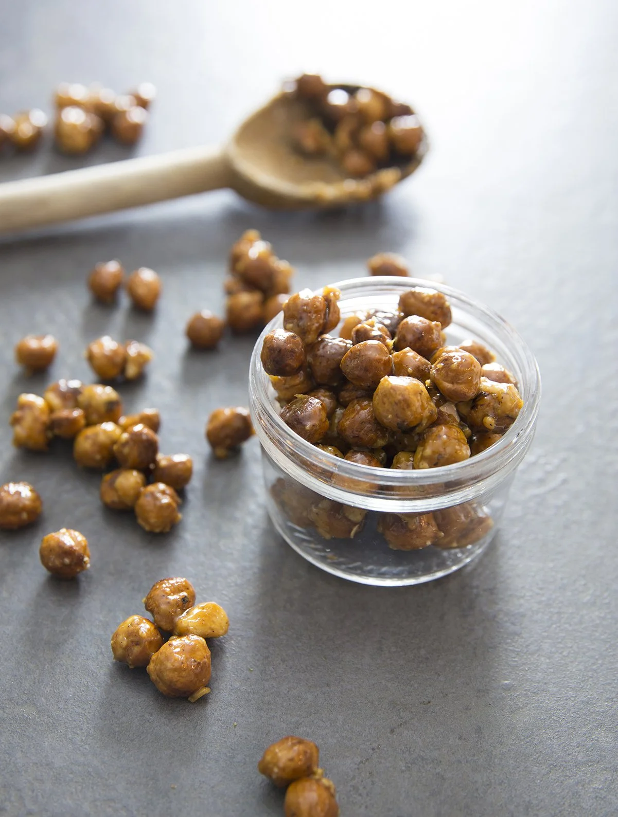 Roasted and caramelized whole hazelnuts in jar, with wooden spoon. 