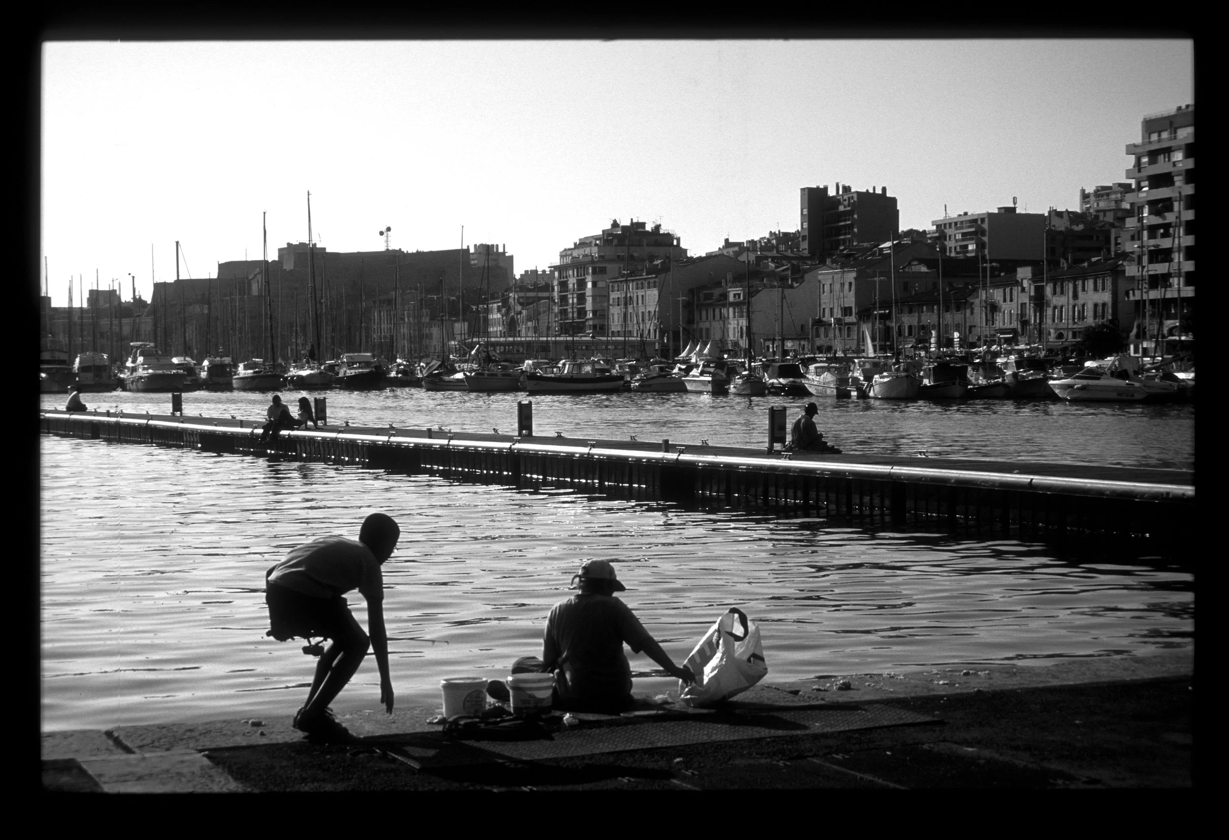 Children in silhouette on the docks in Marseille, France. Black and white travel photography with striking composition 