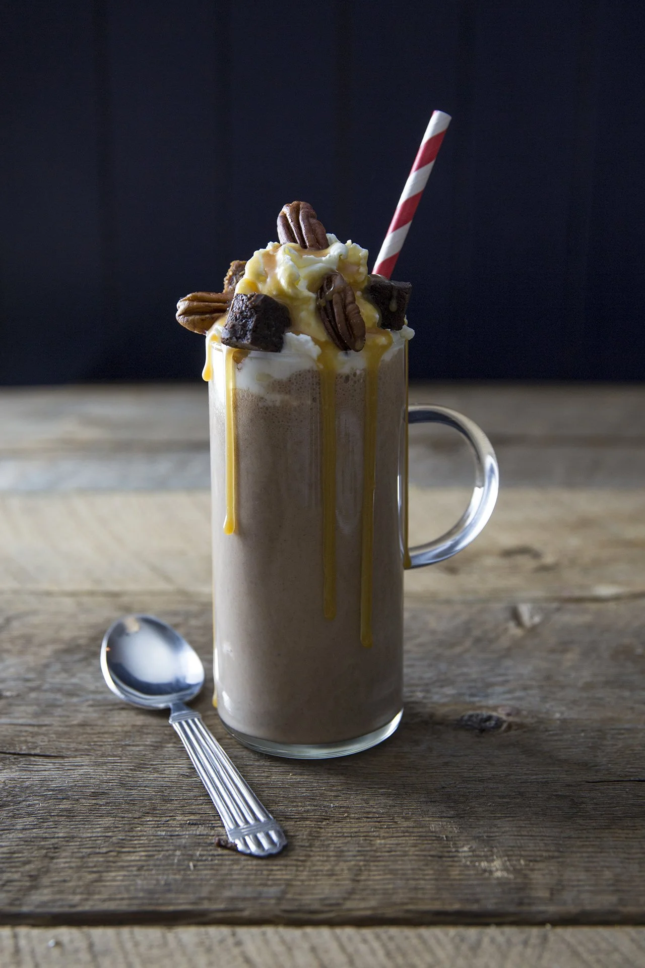 Yummy chocolate drink in tall glass, with red and white straw, whipped cream and roasted pecans. 