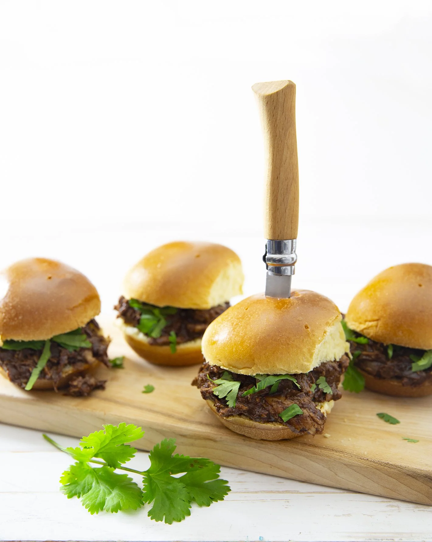 Cocoa pulled pork sliders on wooden serving board with knife through a slider and coriander leaves