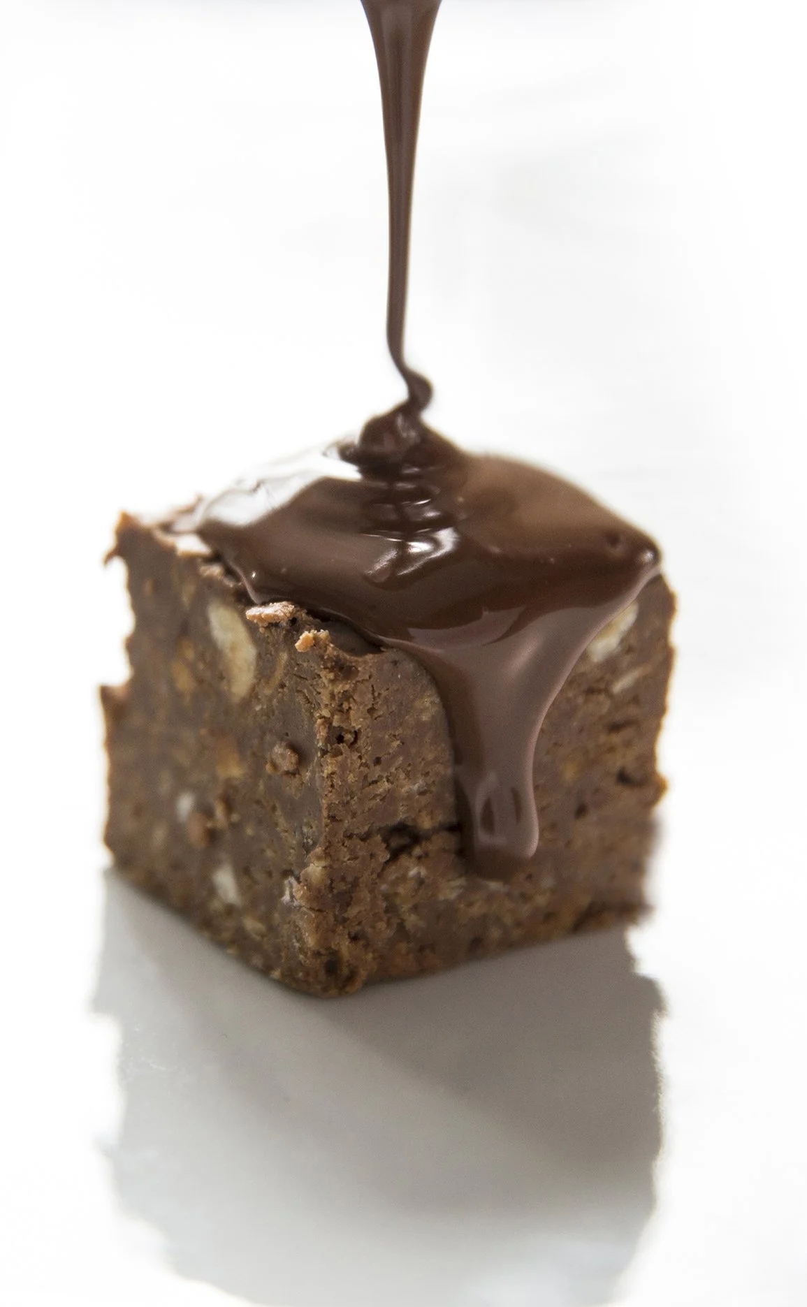 Milk chocolate confection with melted chocolate pouring on top on white background