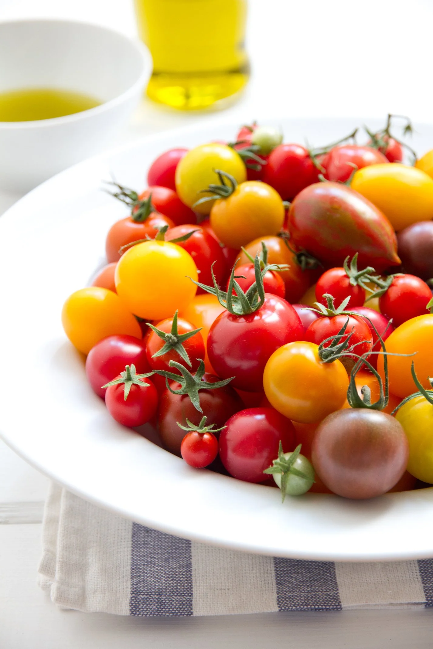 Bowl of heirloom cherry tomatoes in red, yellow, and orange, with olive oil in the background.