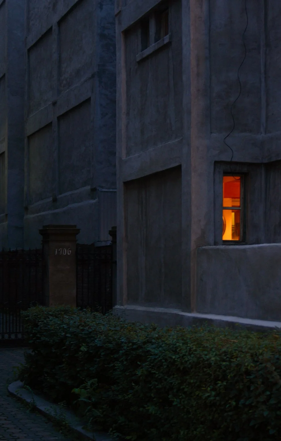 Striking blue and red composition with a single lit window at night, moody and mysterious color  photography
