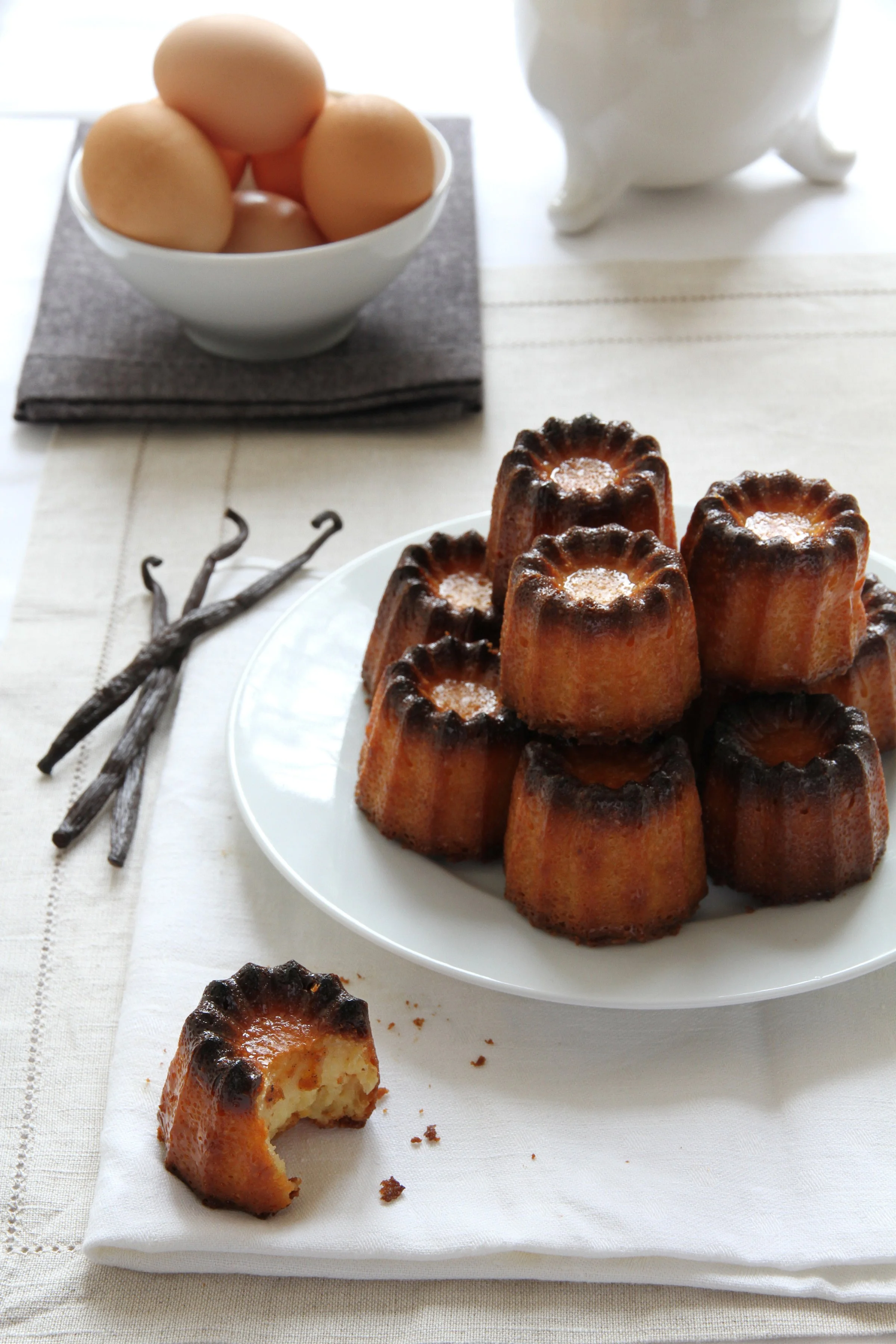 French canneles on a white plate in the kitchen with vanilla bean pod, elegant food photography