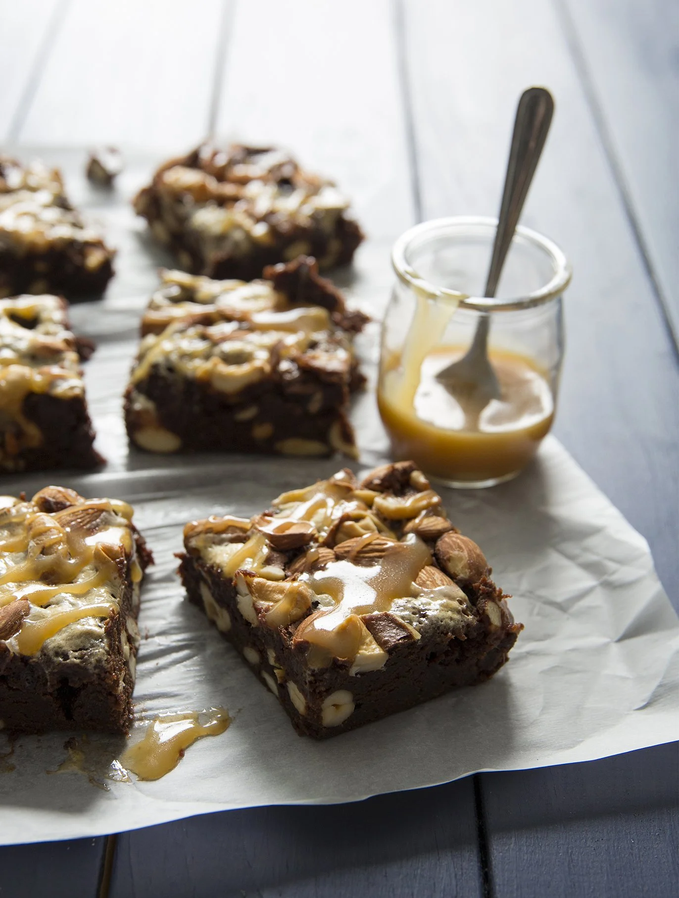 Nut and caramel dark chocolate brownie, drizzled with shiny salted caramel on top, on blue wooden serving board
