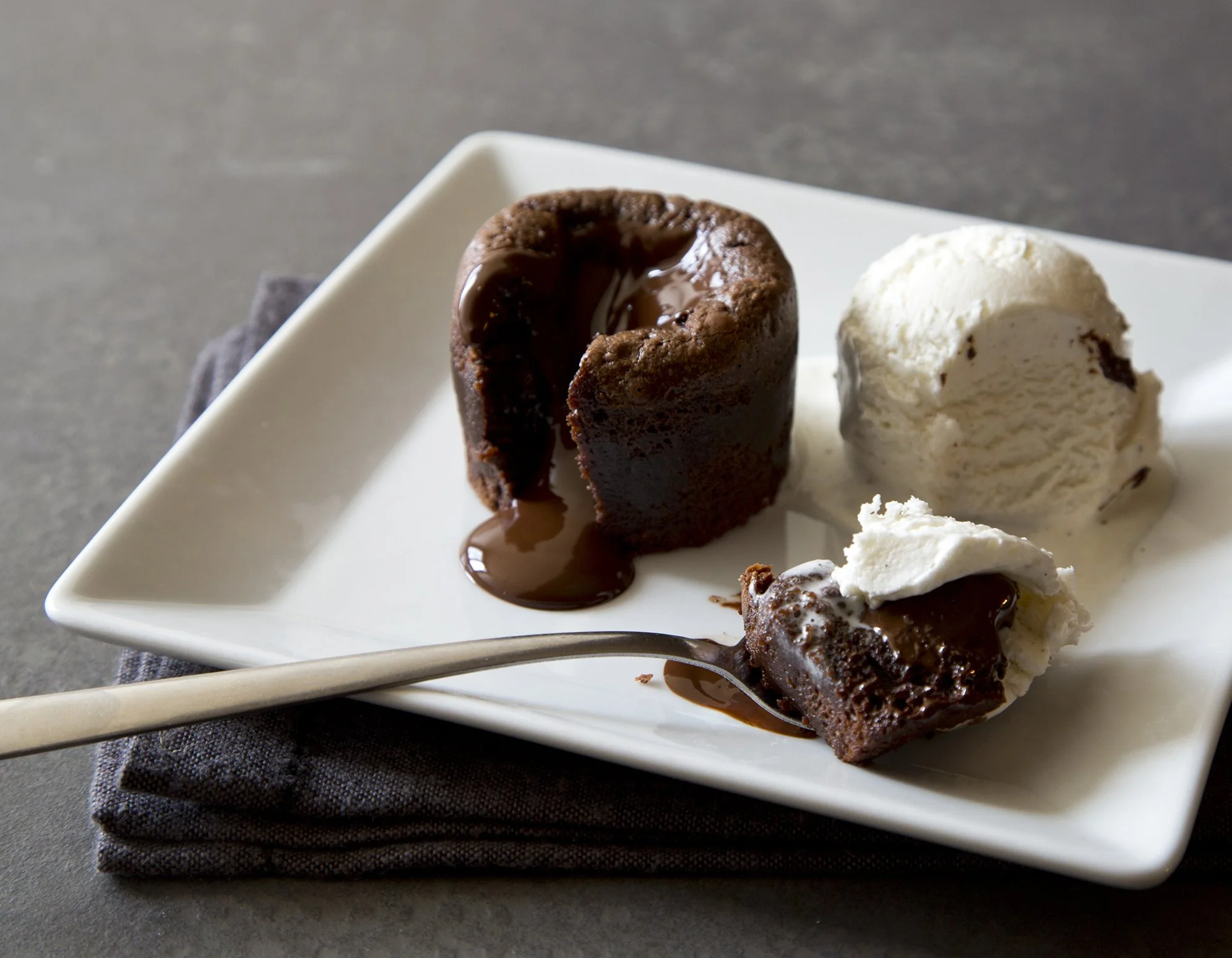 A dark chocolate lava cake with flowing chocolate heart and a scoop of vanilla ice cream on white plate