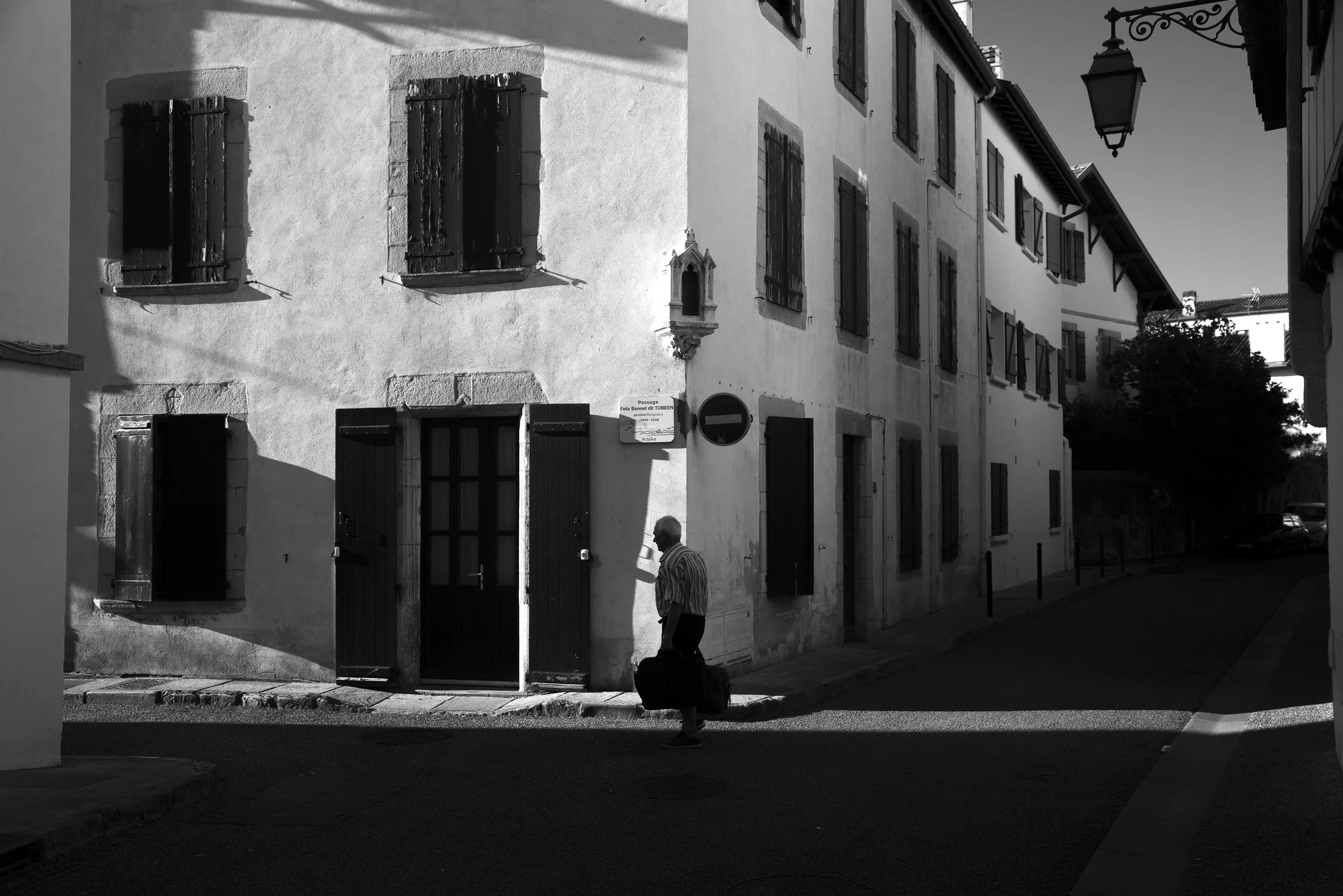 Man walking along the streets in black and white, slanted shadows and sunlight in St-Jean de Luz, France. 