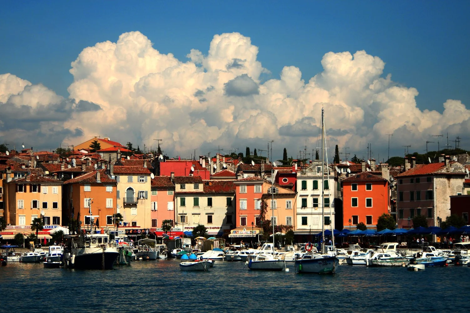 A colorful view of the harbor of Kotor, with rows of yellow, pink and red houses, beautiful wide sky with puffy white clouds, saturated color slide photography