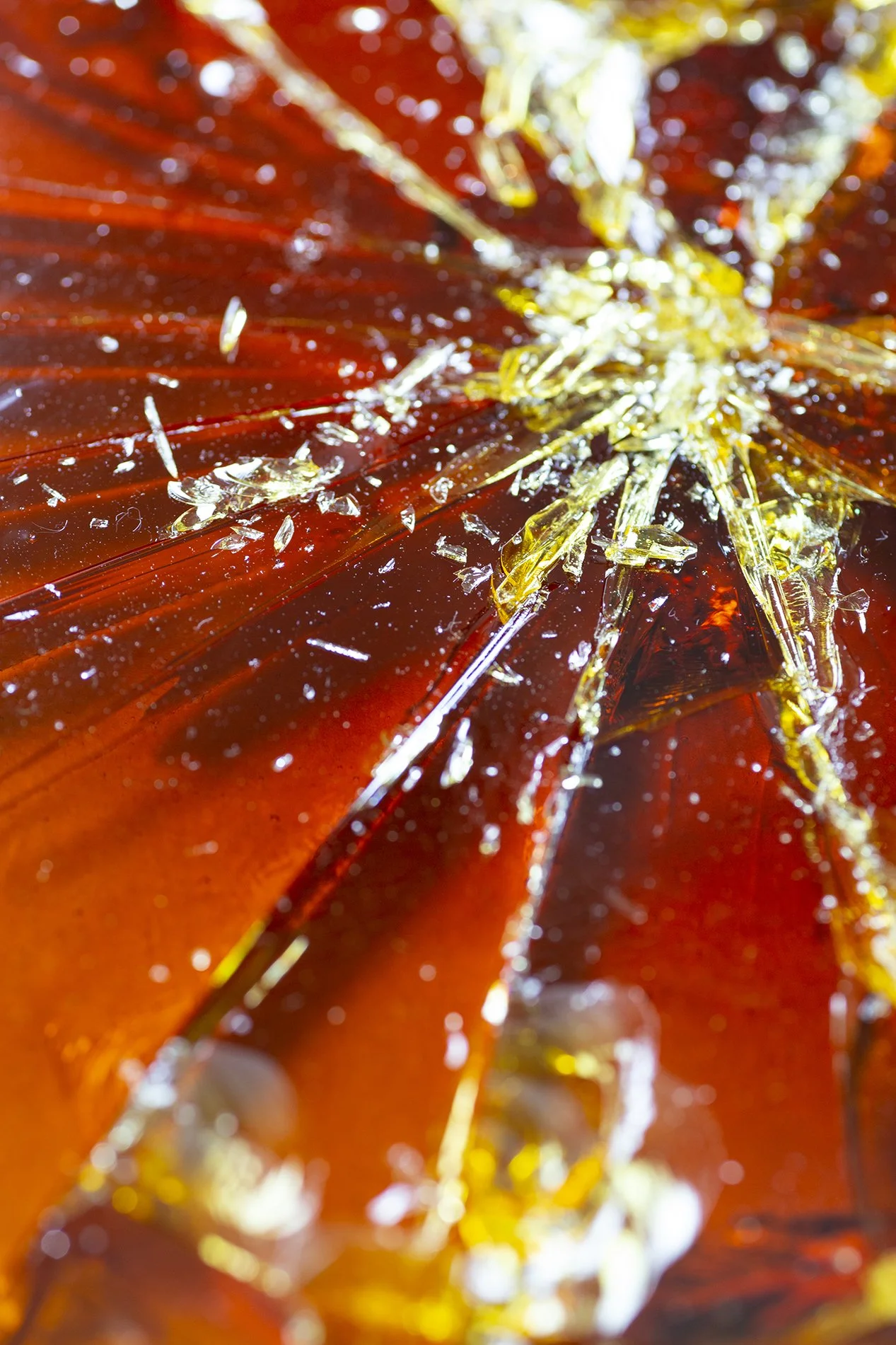 Extreme close-up of shattered amber caramel, cracks radiating out like a spider web of glass.
