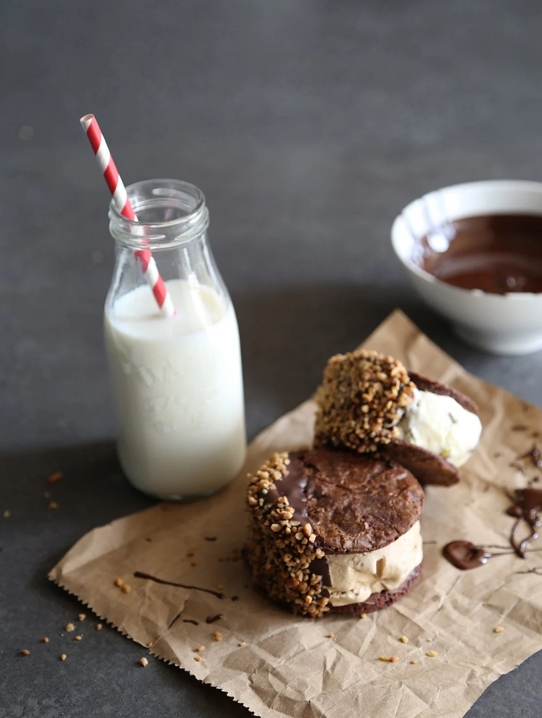 Ice cream sandwiches made with two round brownies and dipped in chocolate, with a bottle of milk. 