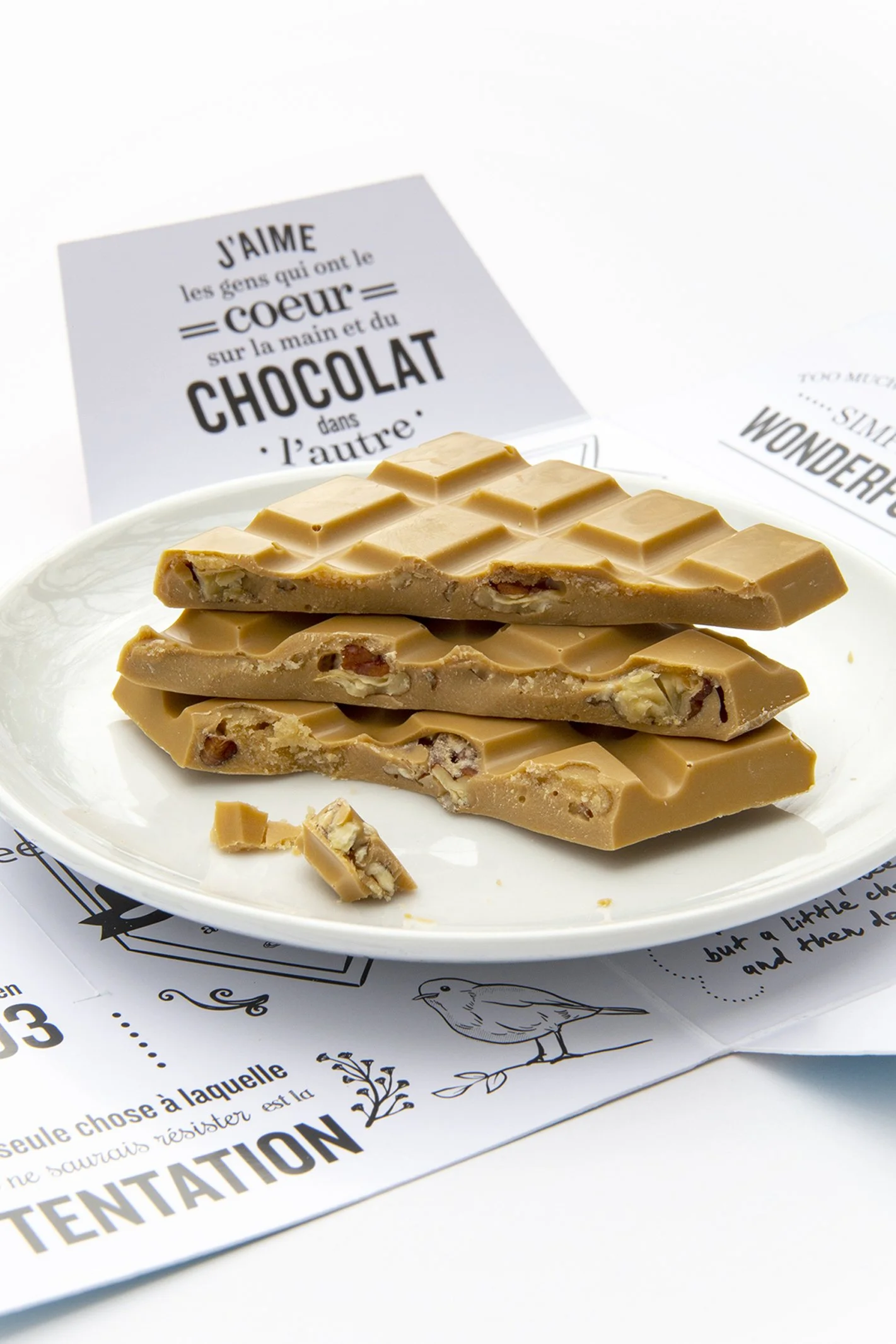 Broken blond chocolate and maple chocolate bar on white plate with packaging. 