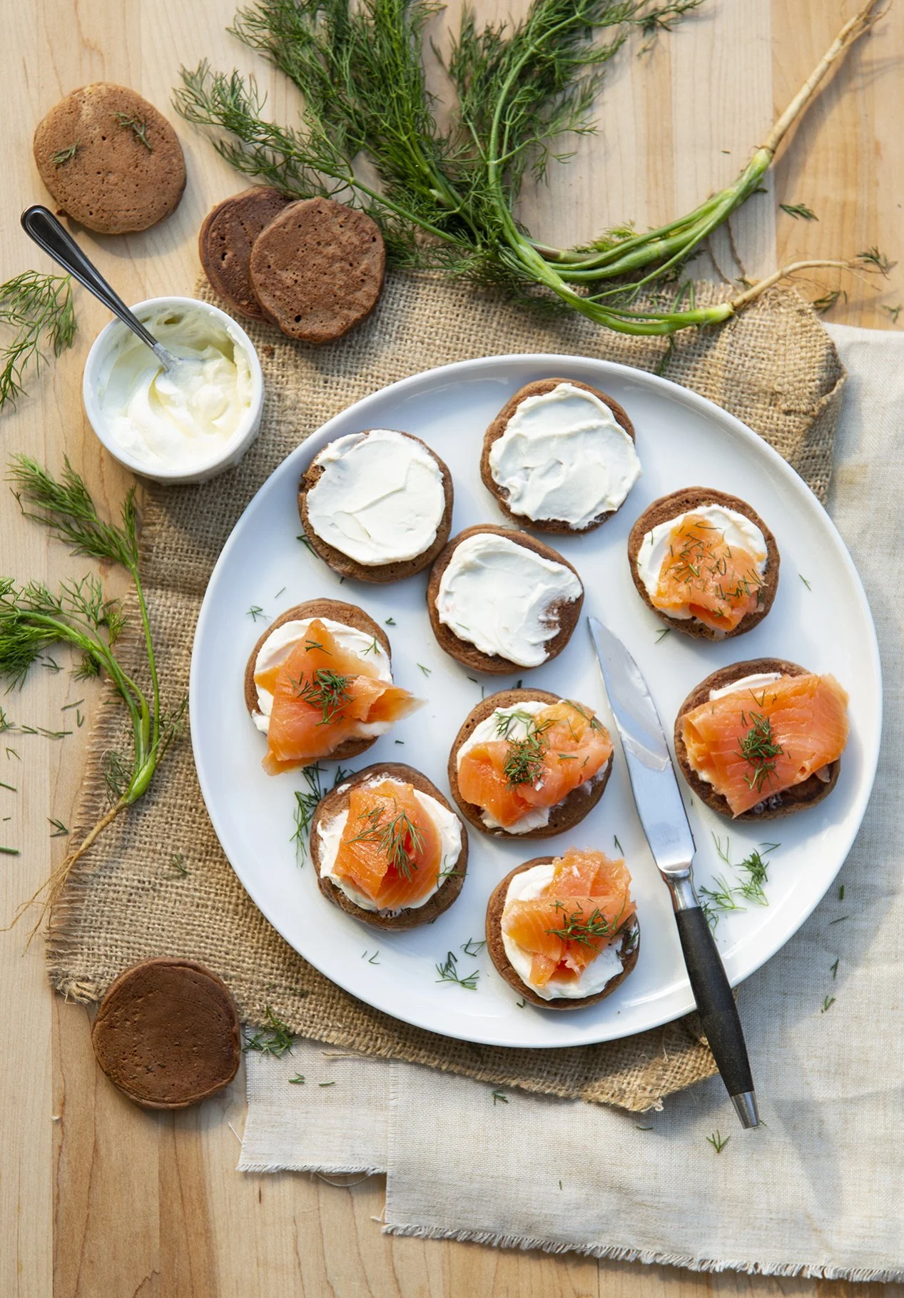 Cocoa blinis with herbed cream cheese and smoked salmon on white plate and rustic wooden table