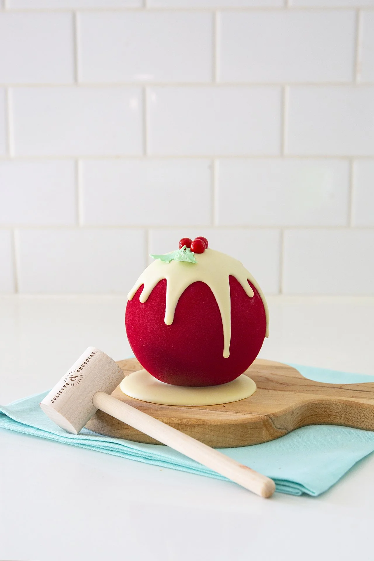 A Christmas chocolate confection, red ornament with white chocolate decoration in the shape of Holly, with small wooden hammer