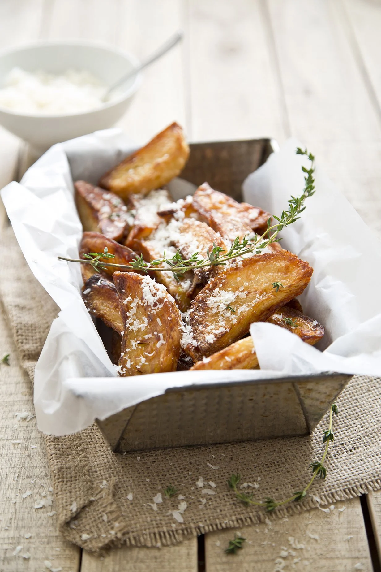 Rustic thick cut home-made fries in a metal serving basket, with a sprig of thyme and a sprinkle of grated cheese