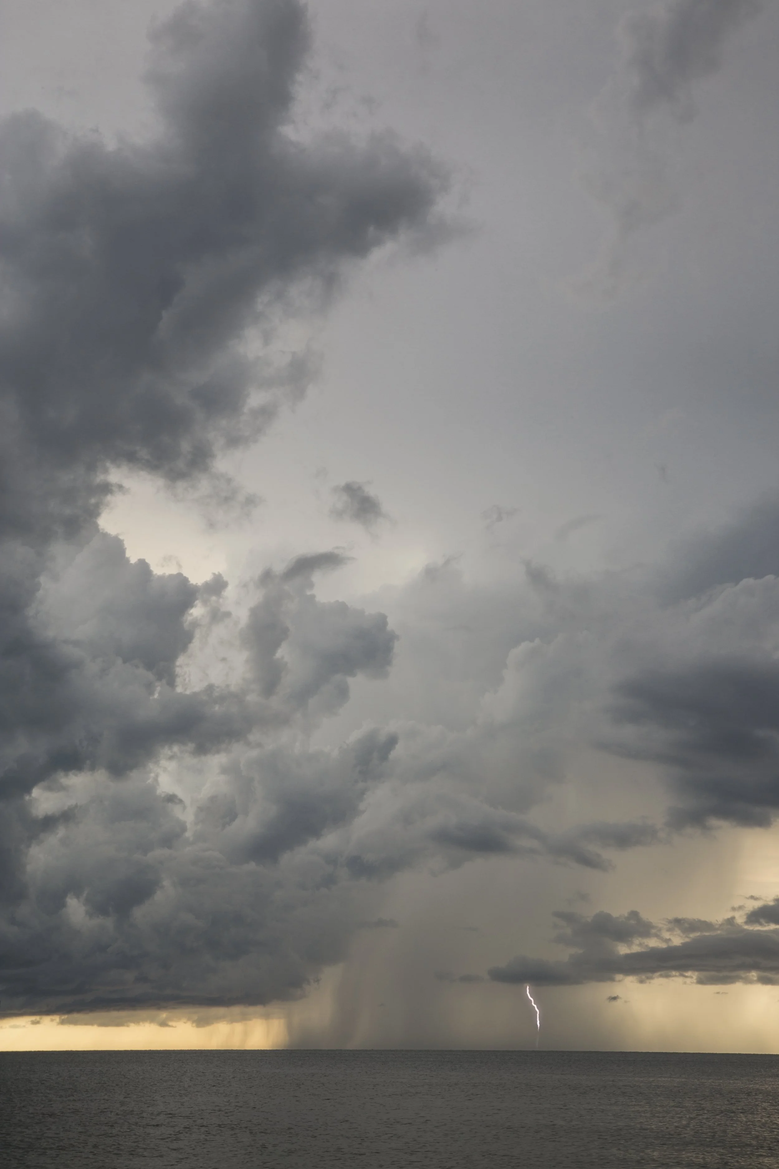 A wide stormy sky with beautiful storm clouds and a single lighting strike in the distance, Naples Florida, wide open vista, ocean and sky