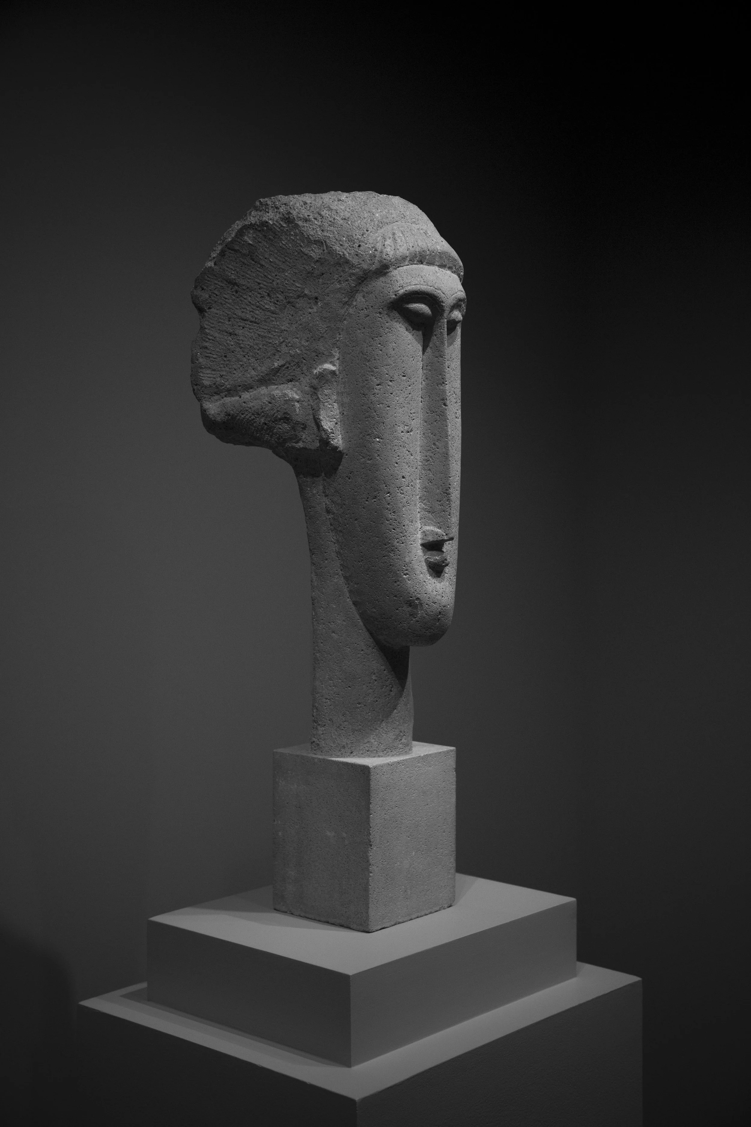 Carved face statue captured in dramatic lighting in museum setting, perfectly composed black and white photo. 