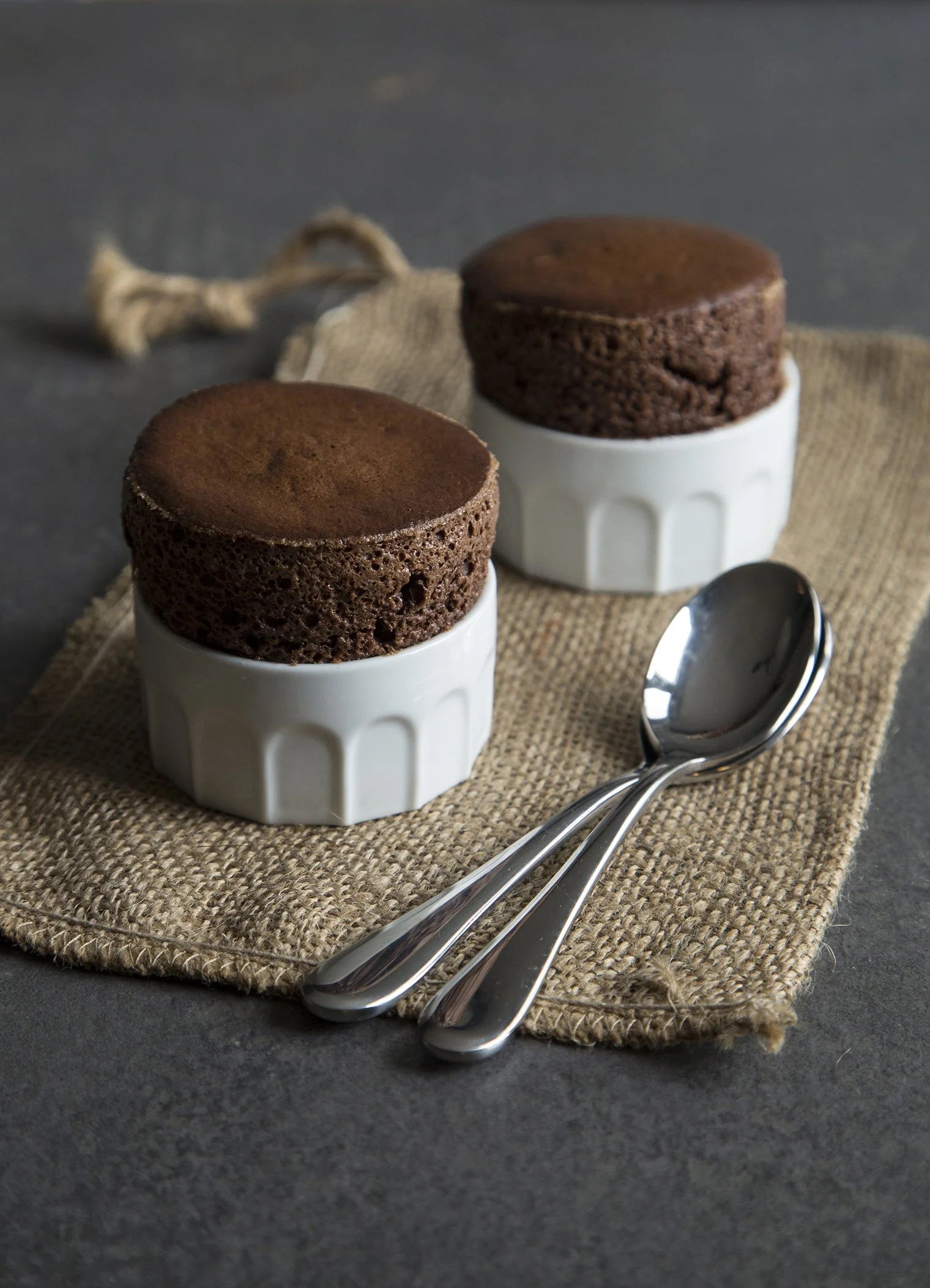 Chocolate souffles in their baking dishes, presented on cloth on ceramic table, monochrome food photo by Lionel May