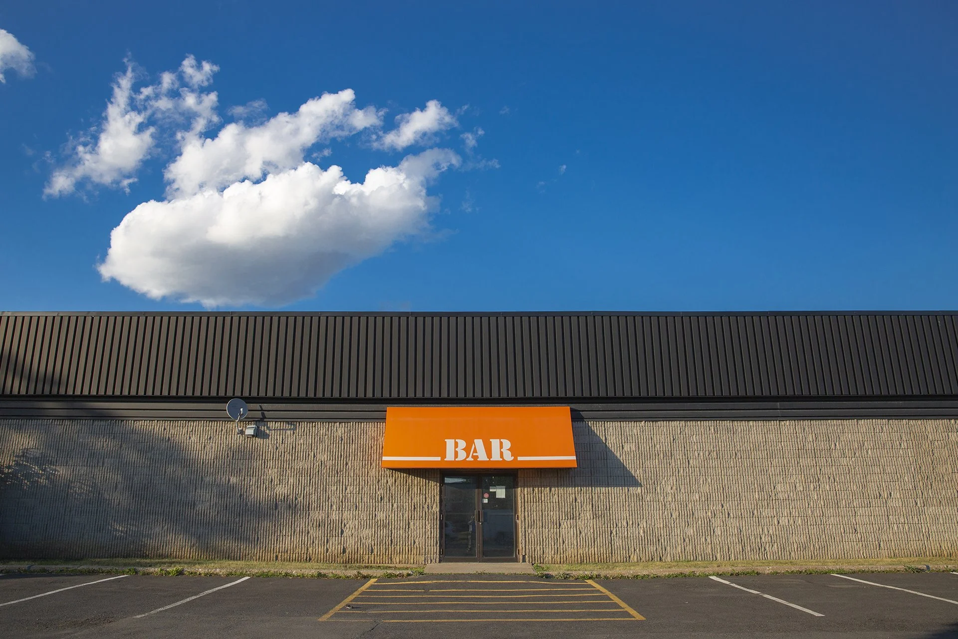 Roadside bar with orange awning under a lone cumulus cloud, part of Lionel May's photography series on suburban vernacular architecture.