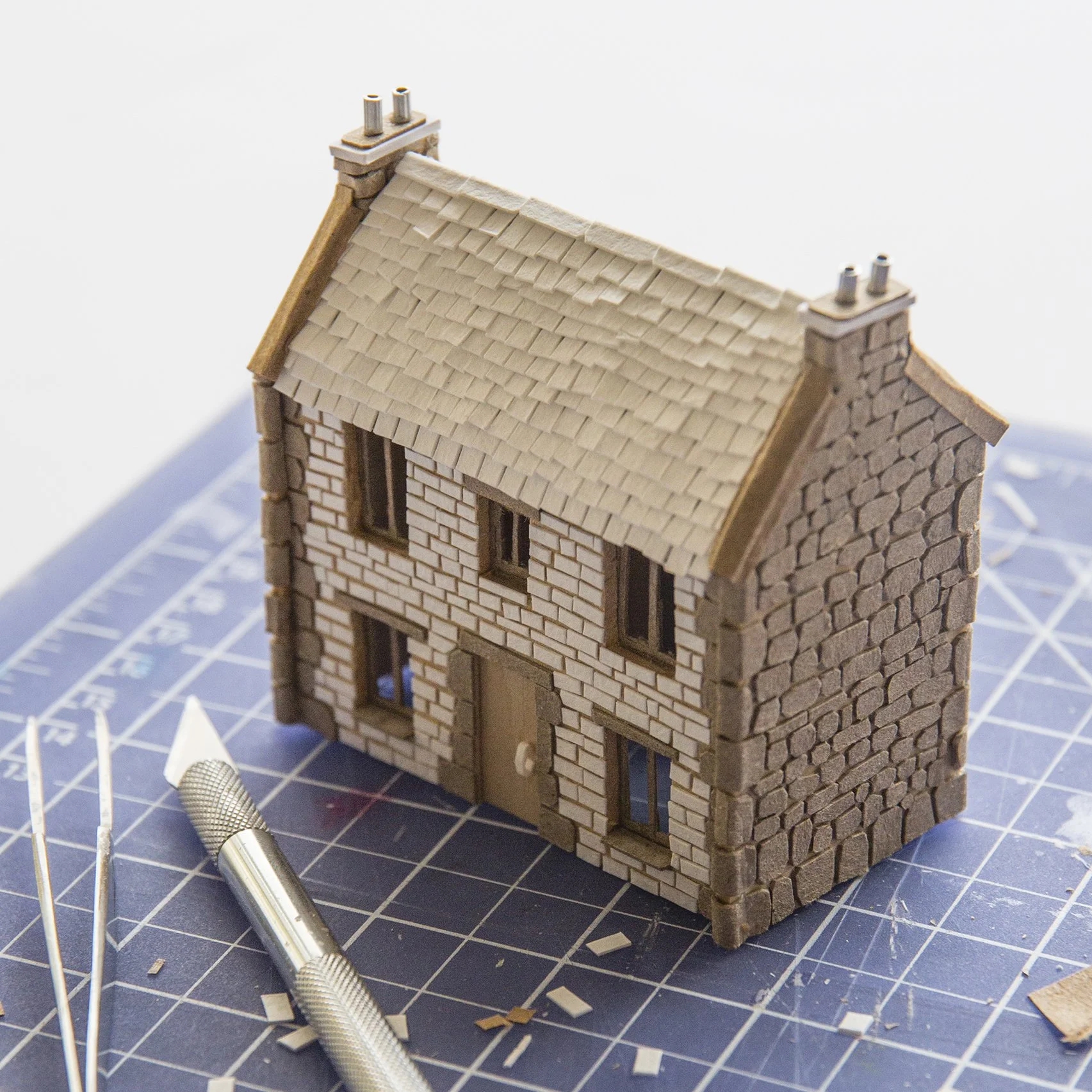 Miniature cardboard and paper house on workbench with cutter and tweezers