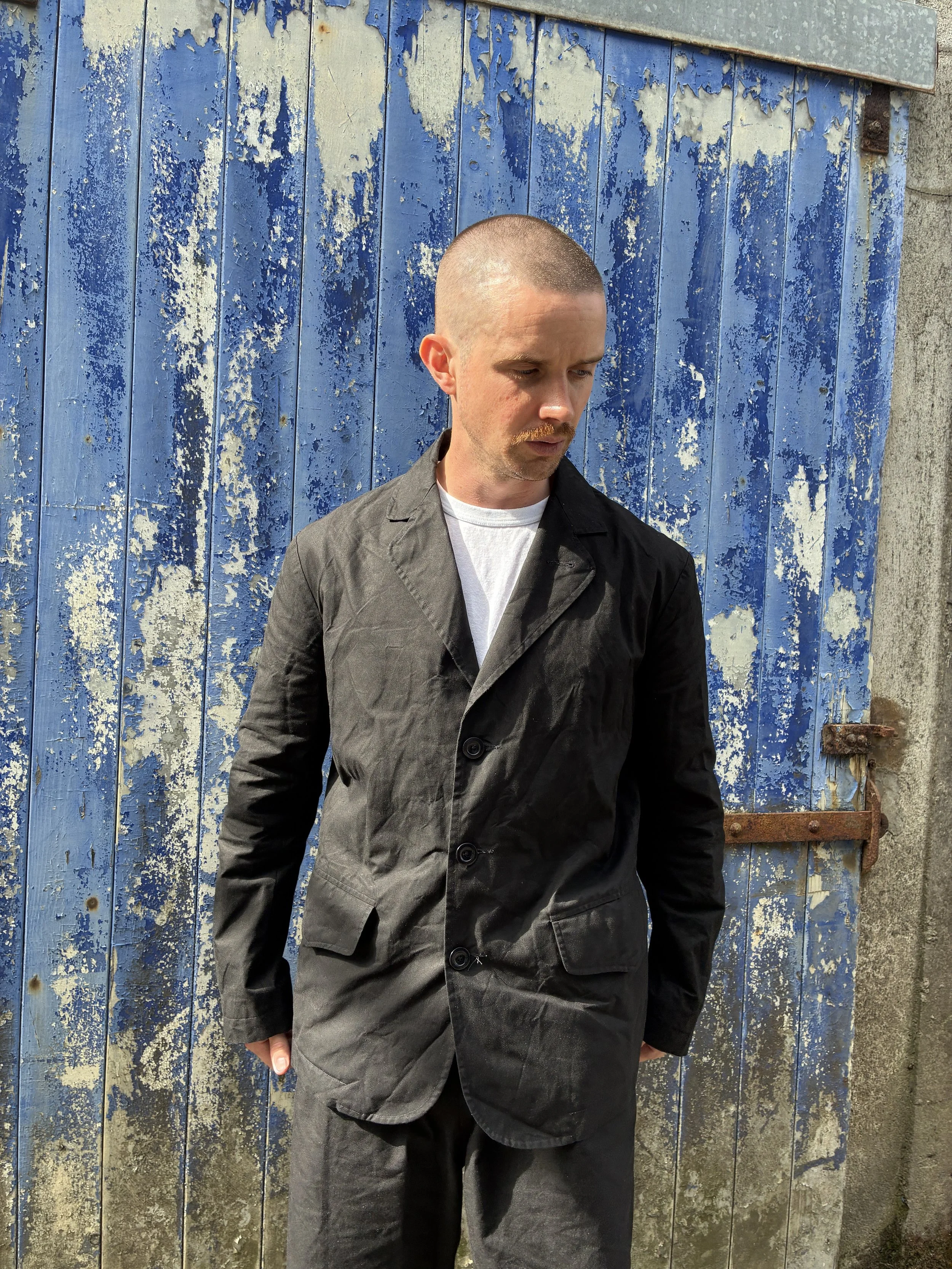 Man in front of blue rusty door outside wearing Black Conkers Rambler Blazer