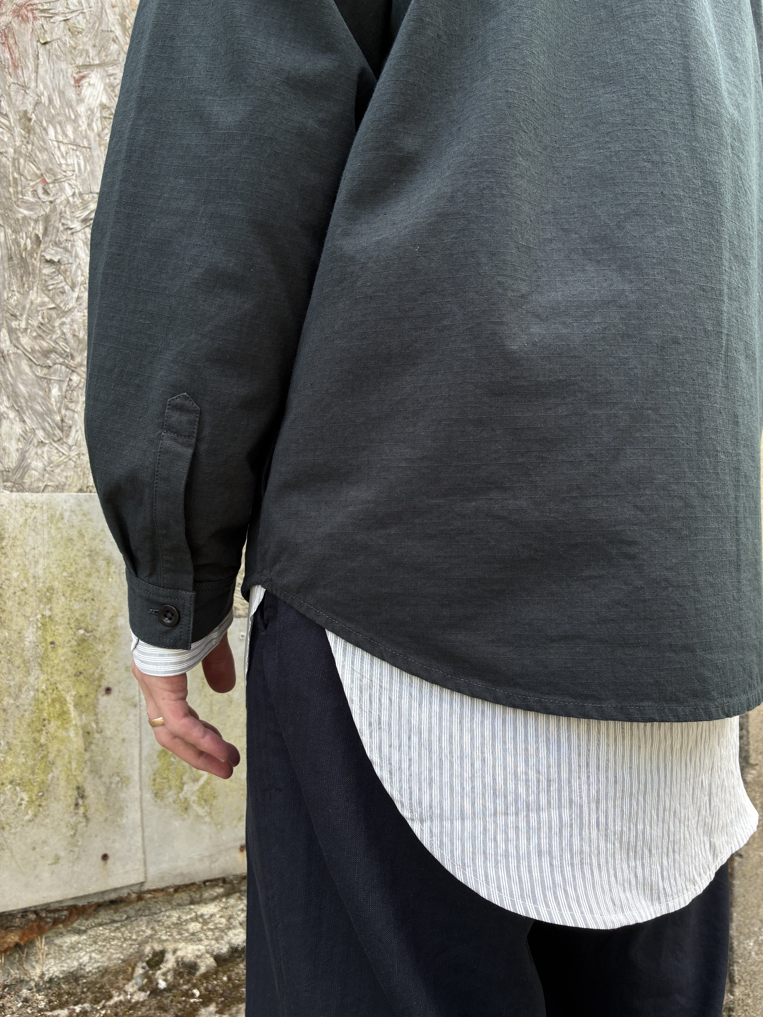 Closeup of hem of Man in front of wall wearing 1st PAT-RN Sumatra Charcoal Overshirt