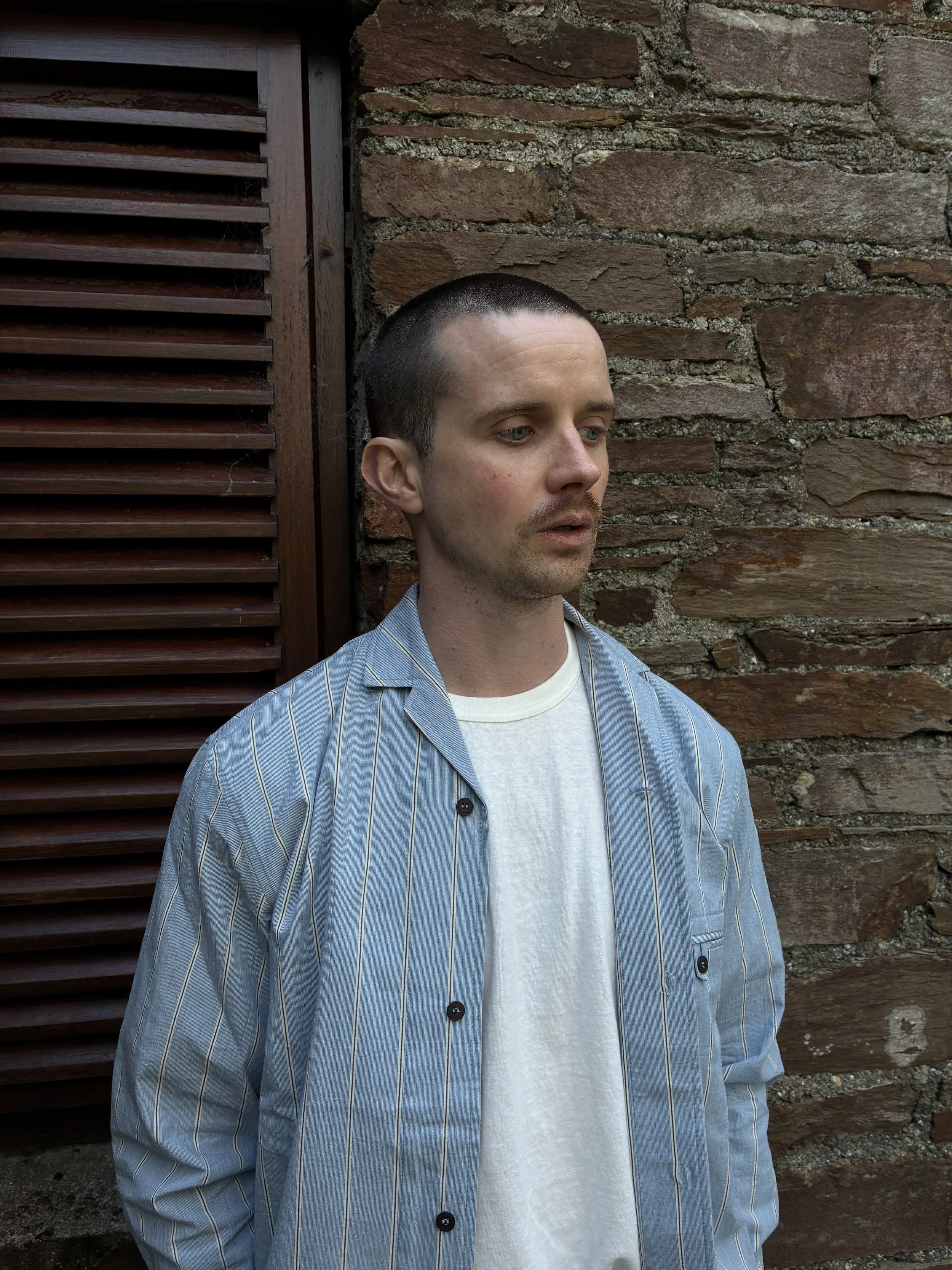 Man wearing open Frank Leder Japanese Cotton Blue Striped Shirt in front of wall