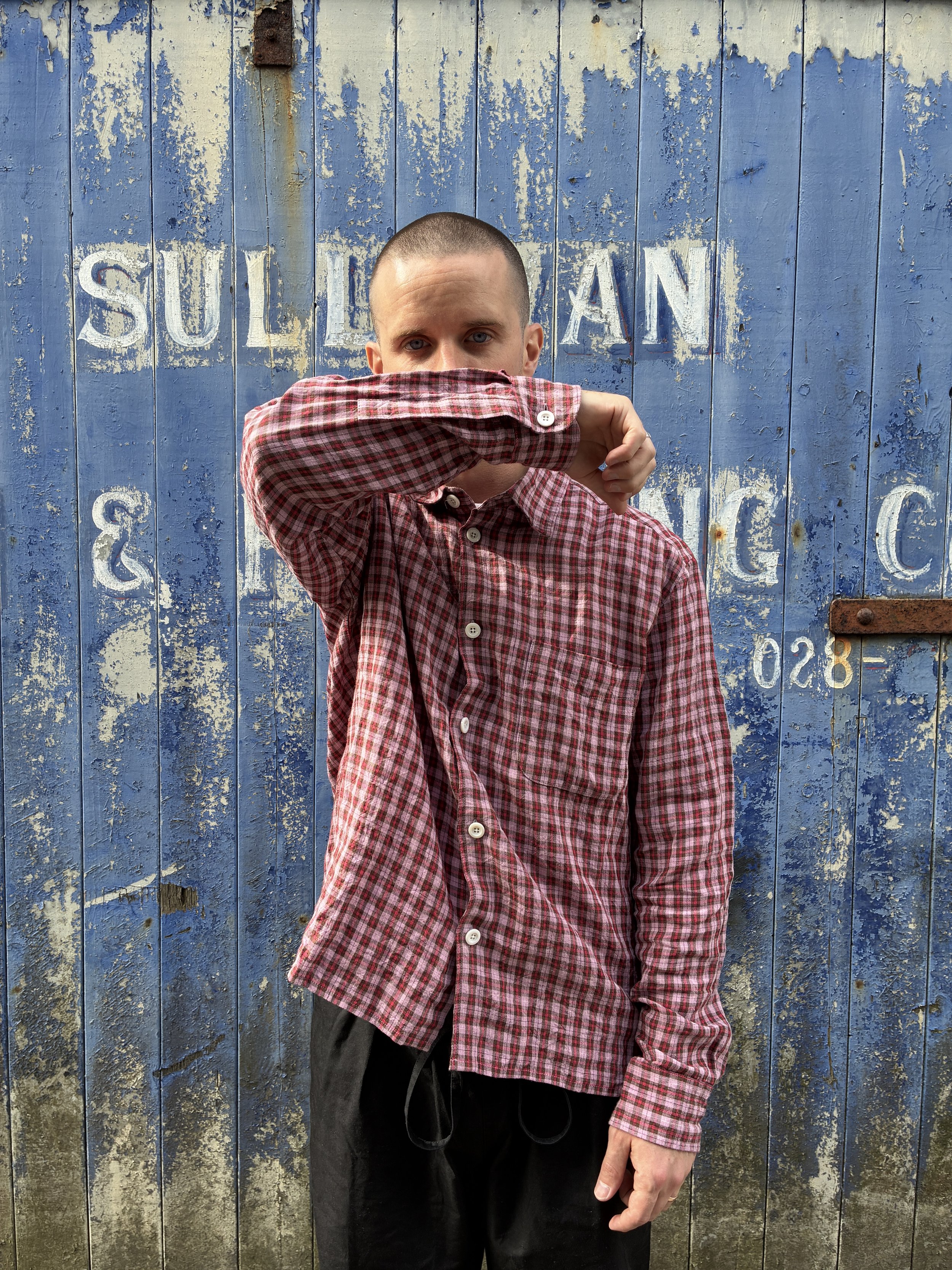 Man wearing Conkers Sunrise Relaxed Farmer Shirt in front of blue shutter with arm over face