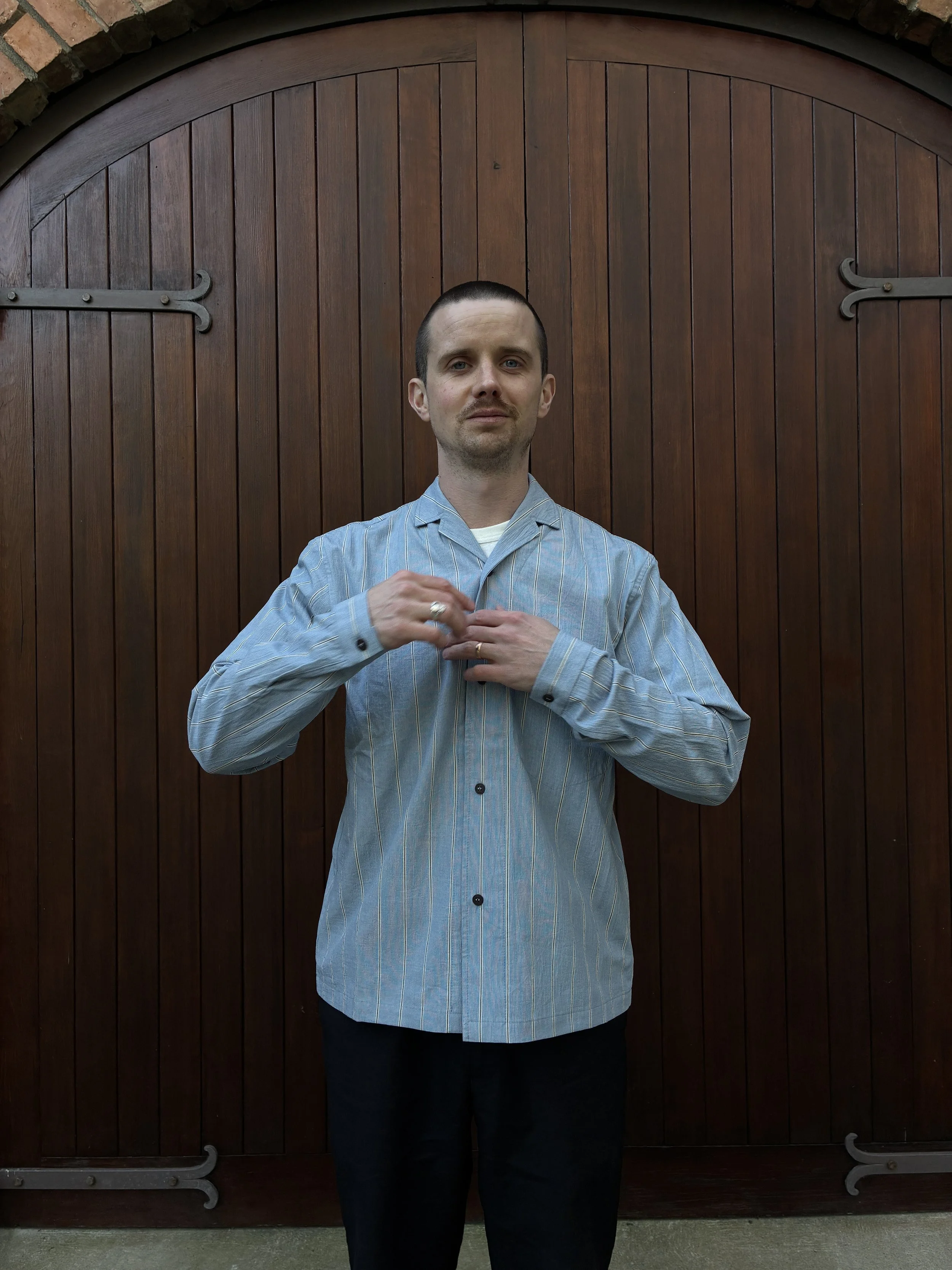 Man buttoning up Frank Leder Japanese Cotton Blue Striped Shirt in front of door