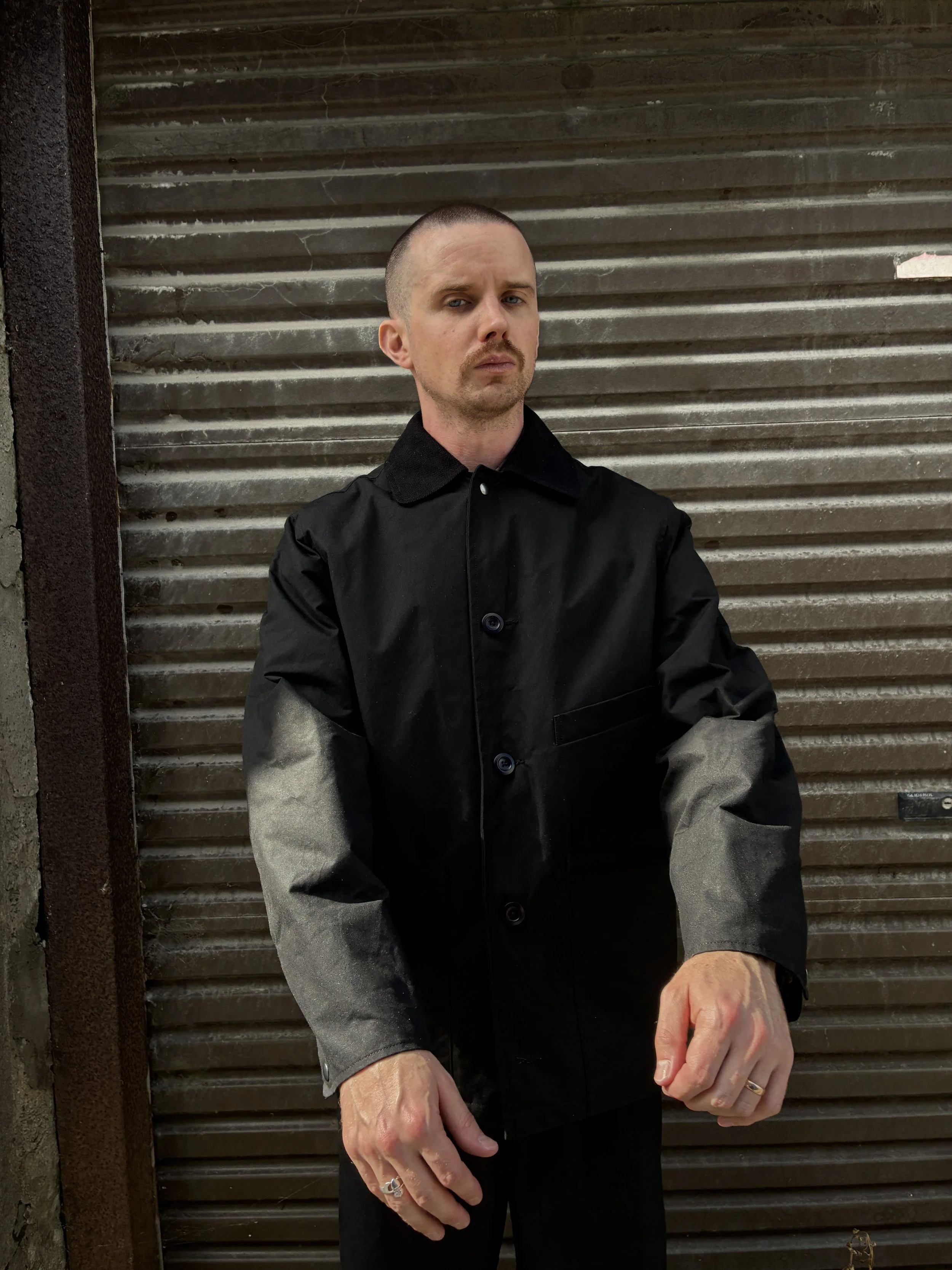 Man wearing Black Conkers Blanket Jacket in front of shutters with arms extended