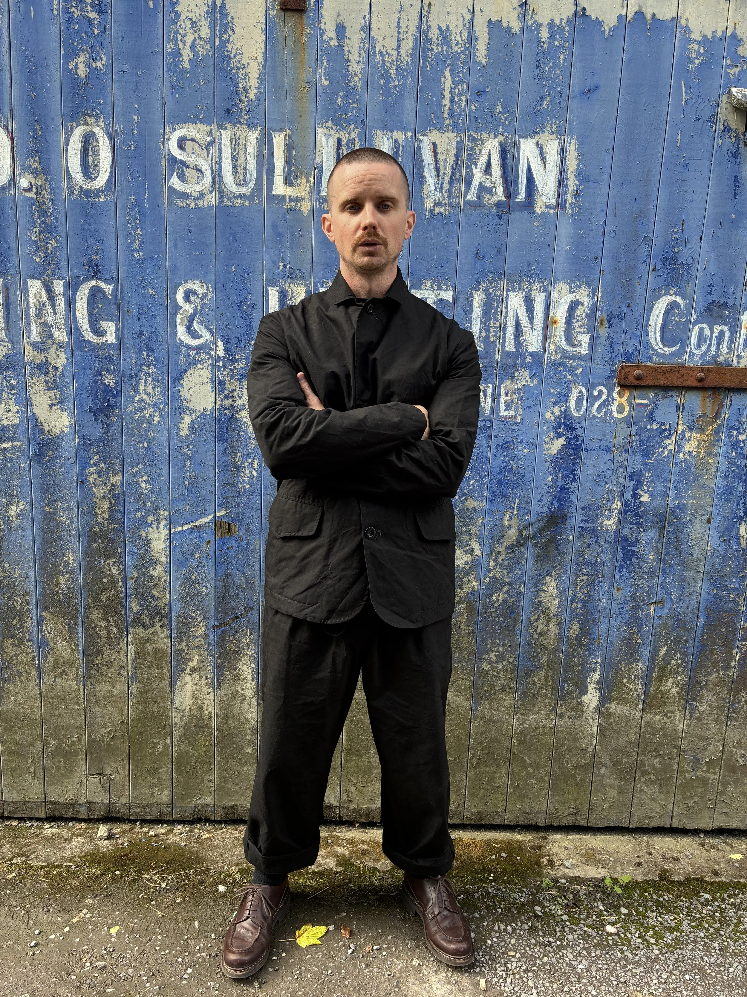 Man in front of blue rusty door outside wearing Black Conkers Rambler Blazer and trousers