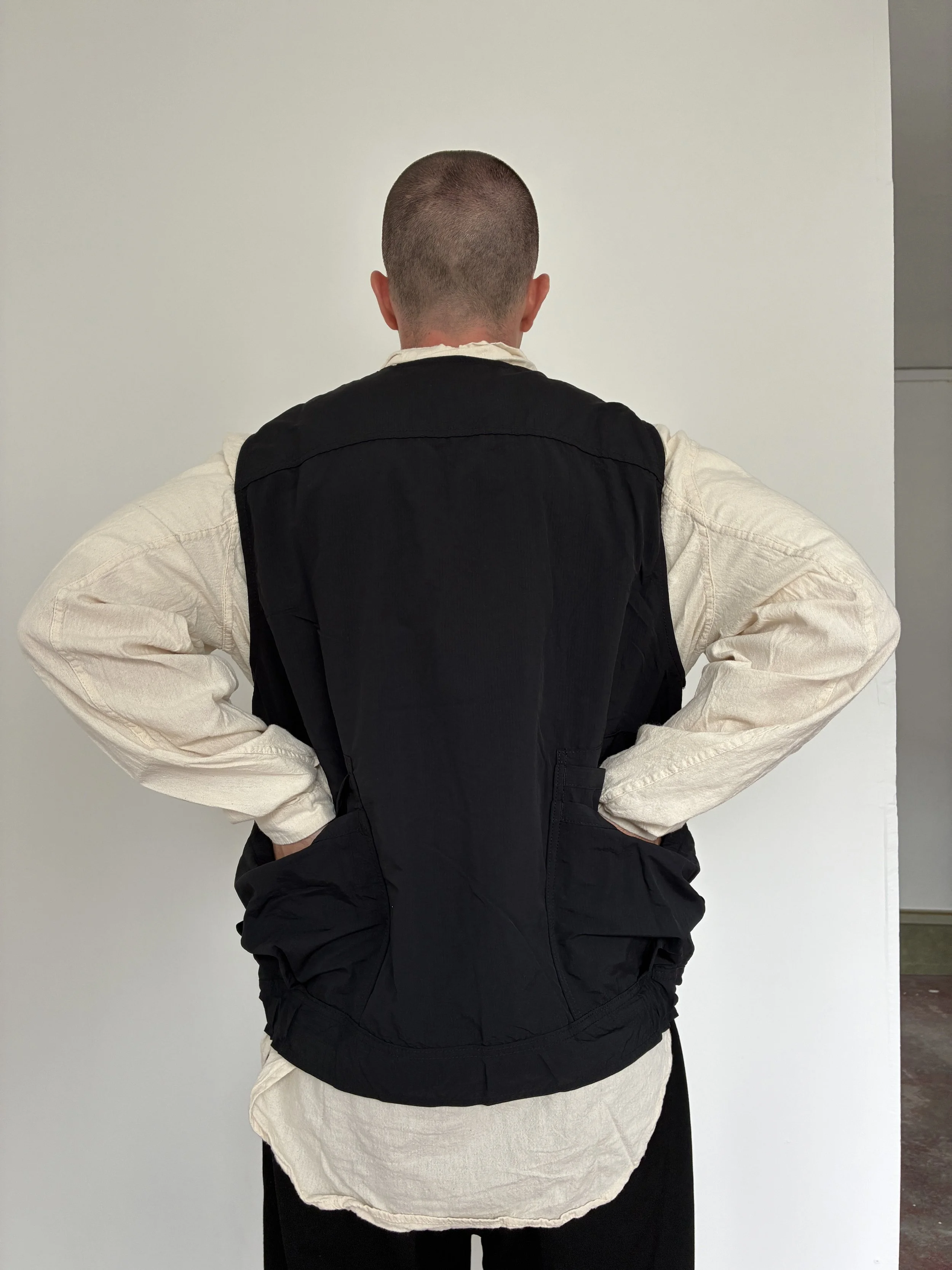 Back of Man wearing Black Sassafras Overgrown Hiker Vest in front of concrete wall