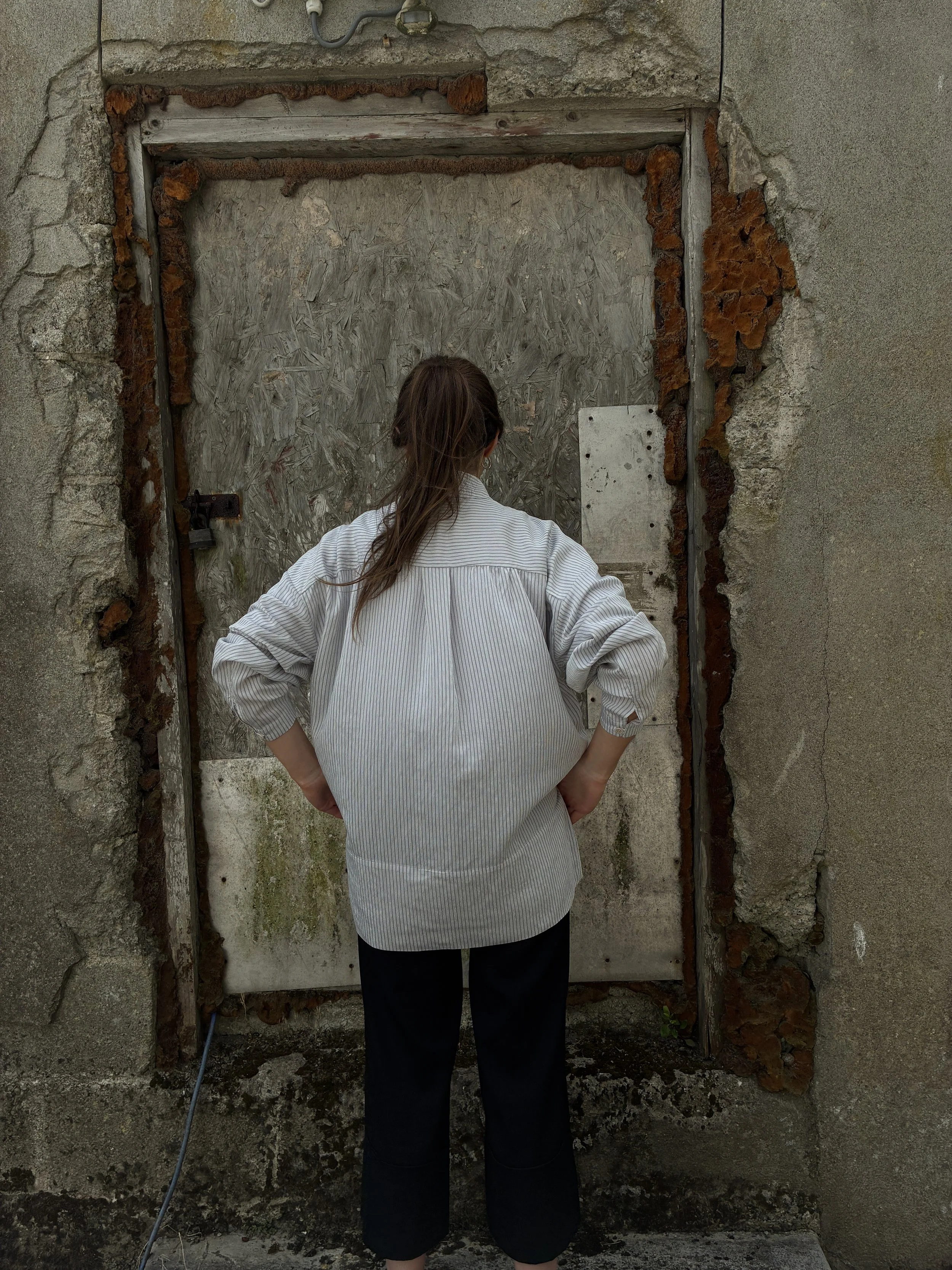 Back of woman in front of wall wearing 1st PAT-RN Woman Modula Shirt in Fine Stripes
