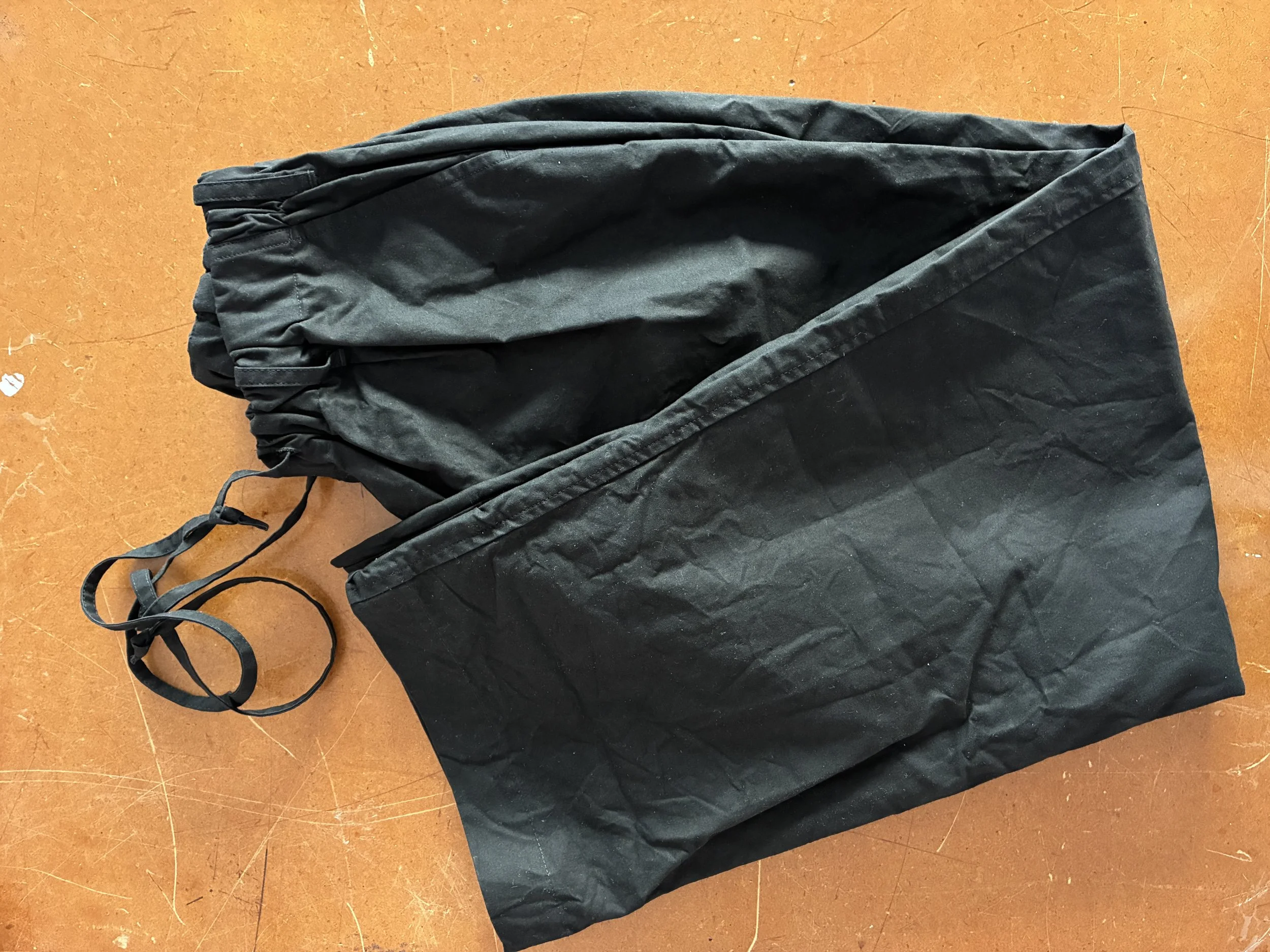 Conkers Rambler Black Waxed Cotton Trousers folded on brown table